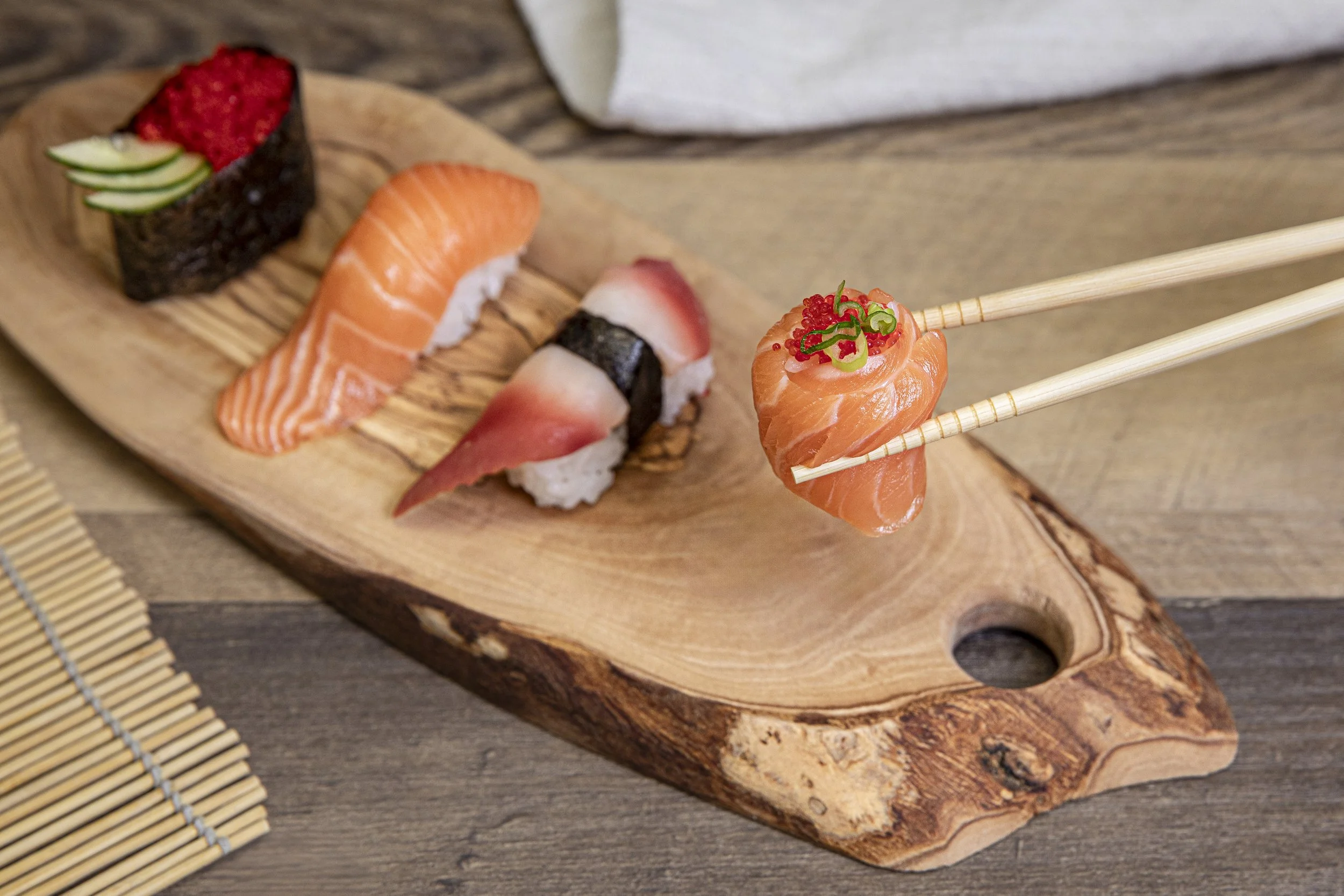 Assorted sushi on a wooden serving board, with a piece held by chopsticks that has salmon, roe, and green onion garnish.
