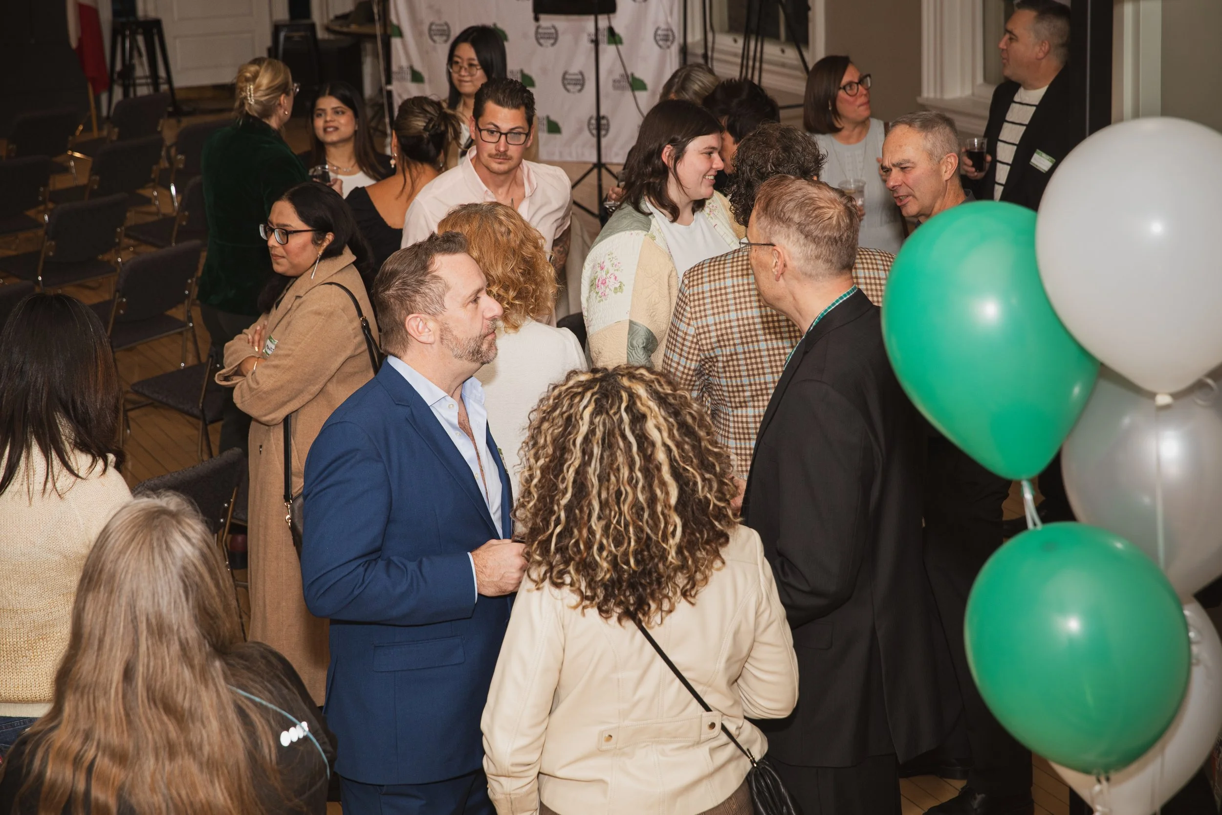 Group of people gathered at a social event, engaging in conversations, with balloons in the foreground.