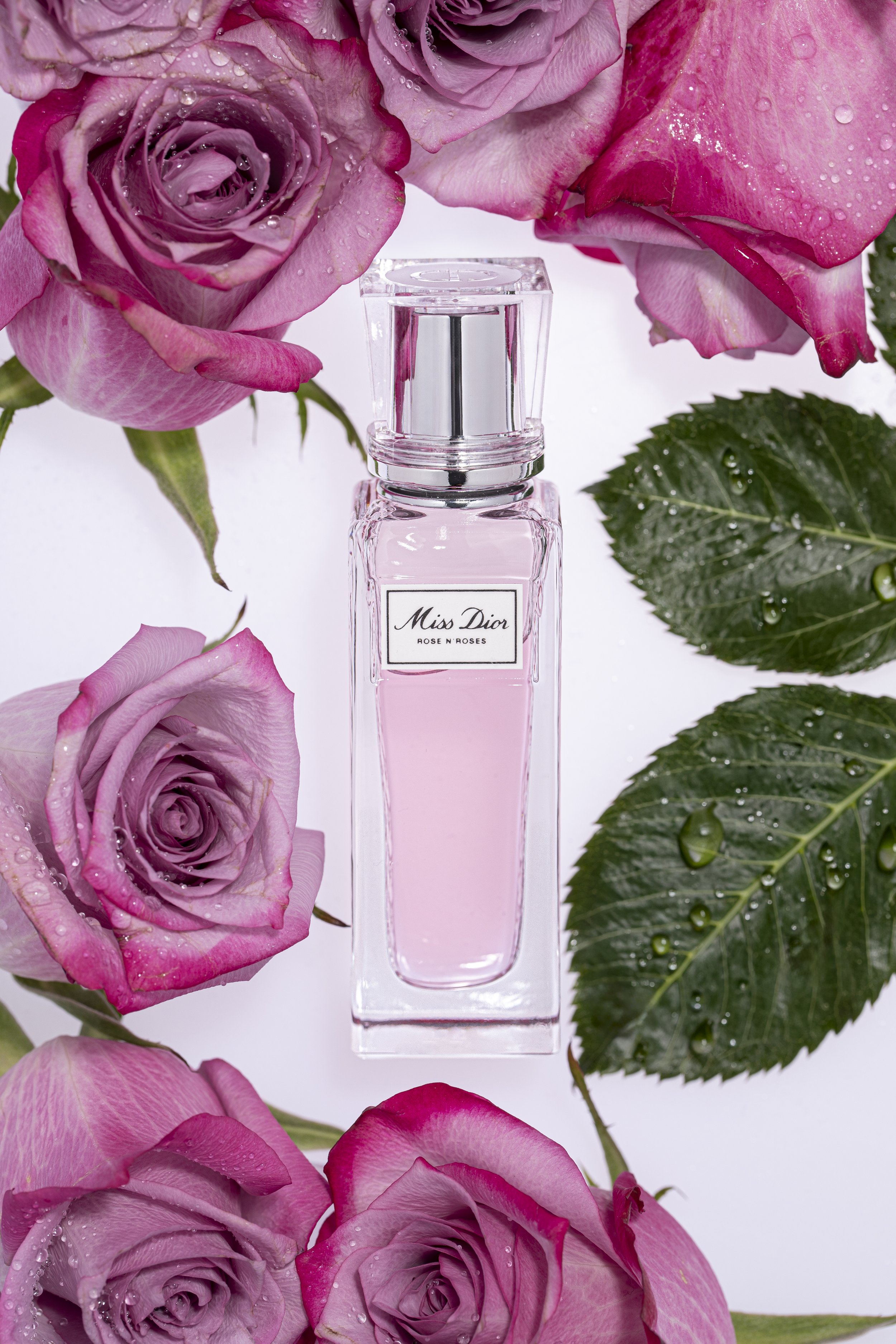 A bottle of Dior fragrance surrounded by red roses with water droplets on their petals.