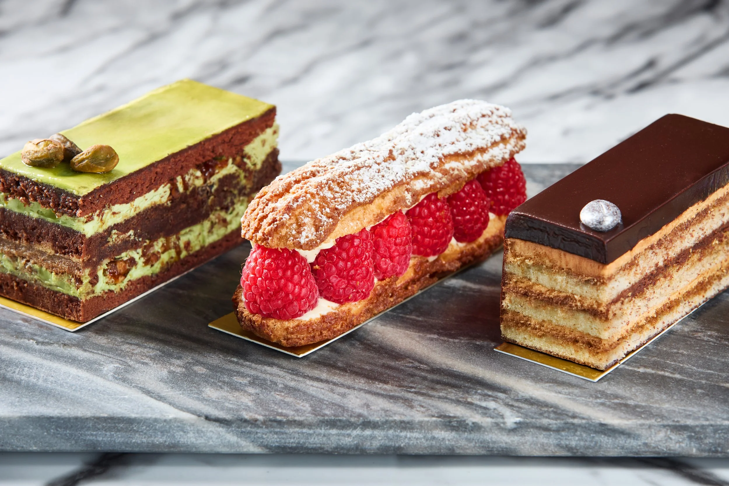 Three assorted layered cakes on a marble surface.