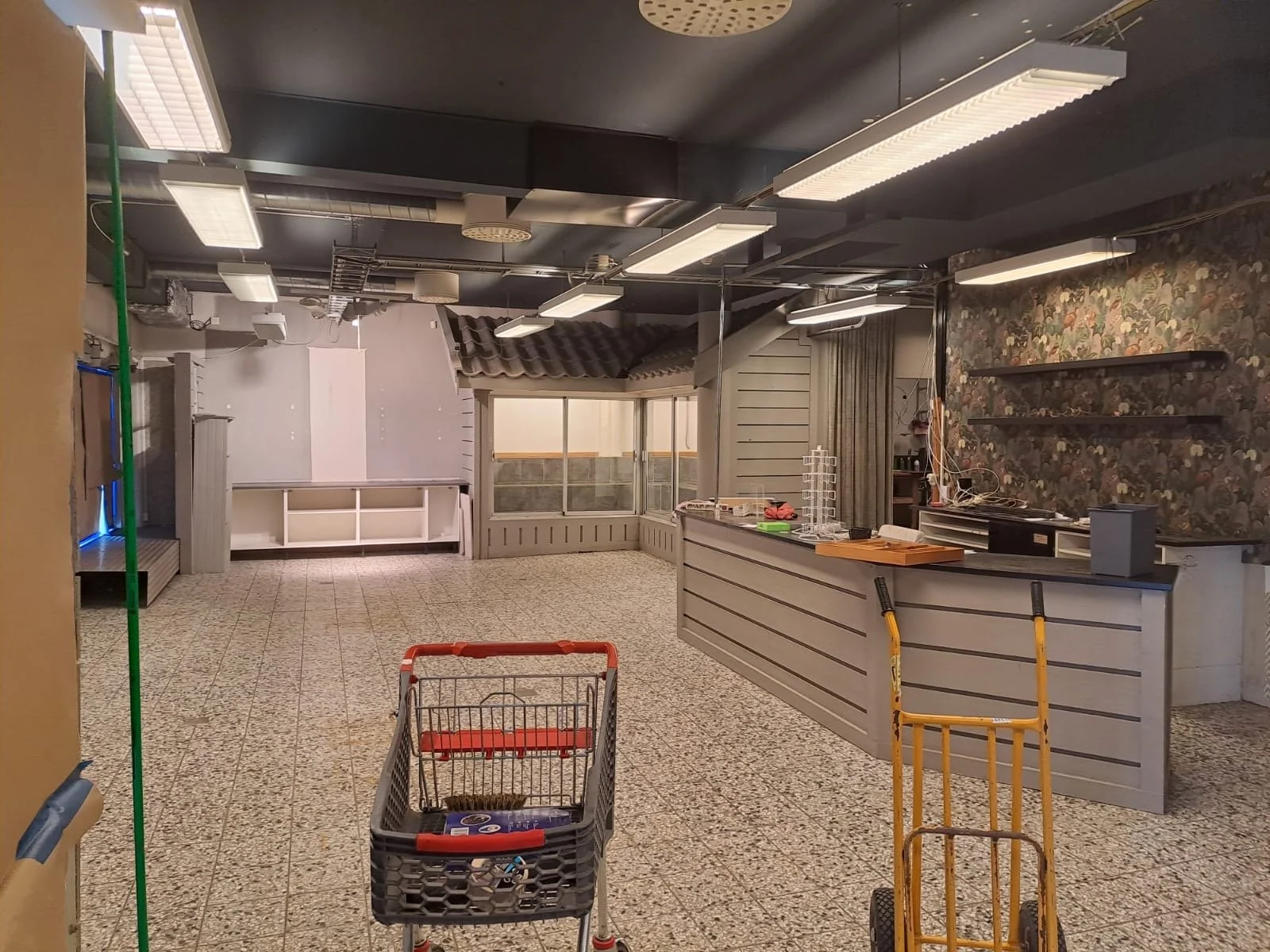 Tomt butiksområde med kassaområde, shoppingvagn, hyllor och belysning.