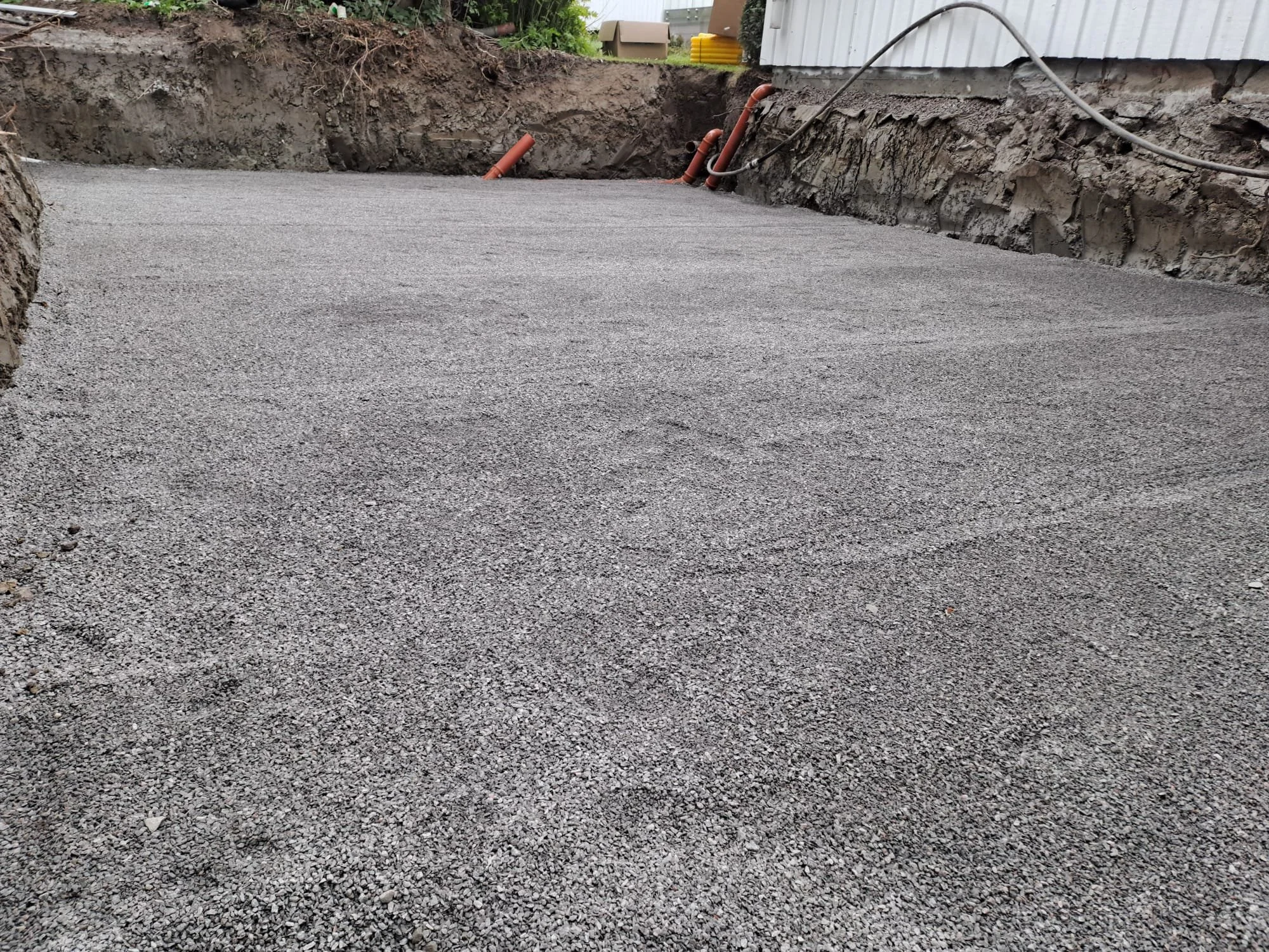 A freshly poured and leveled gravel surface in a construction area with dirt and equipment in the background.