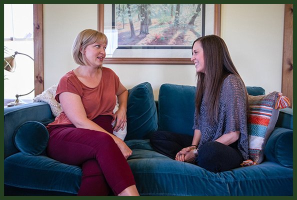 Two women sitting on a blue couch and engaging in individual therapy session in a cozy living room near Asheville