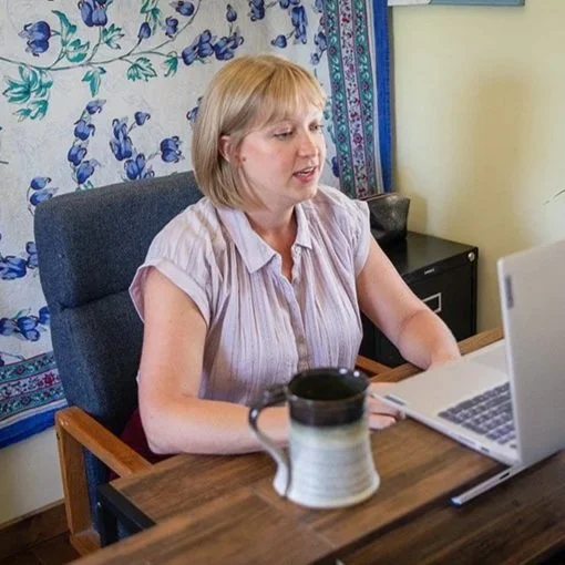 A therapist with blonde hair working on a laptop at a desk, leading a virtual online therapy session in North Carolina