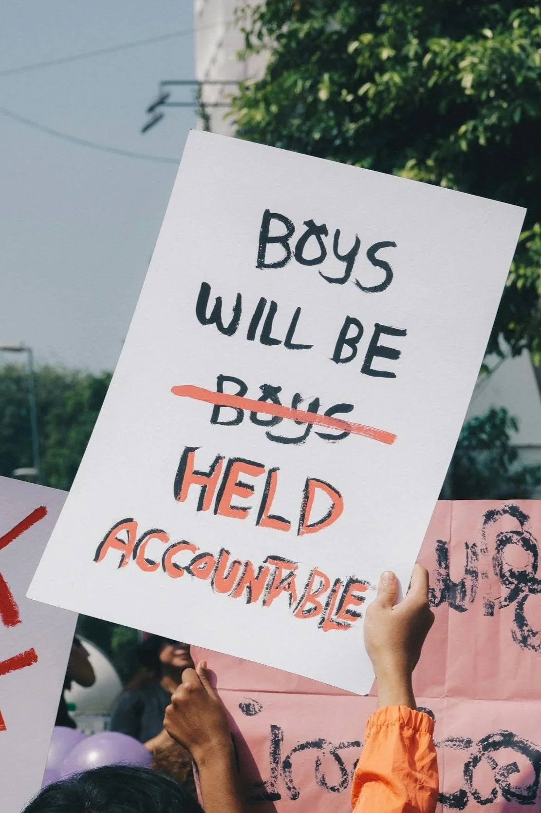 Protest sign that reads "Boys will be boys" but the second boys is crossed out and corrected with "held accountable"