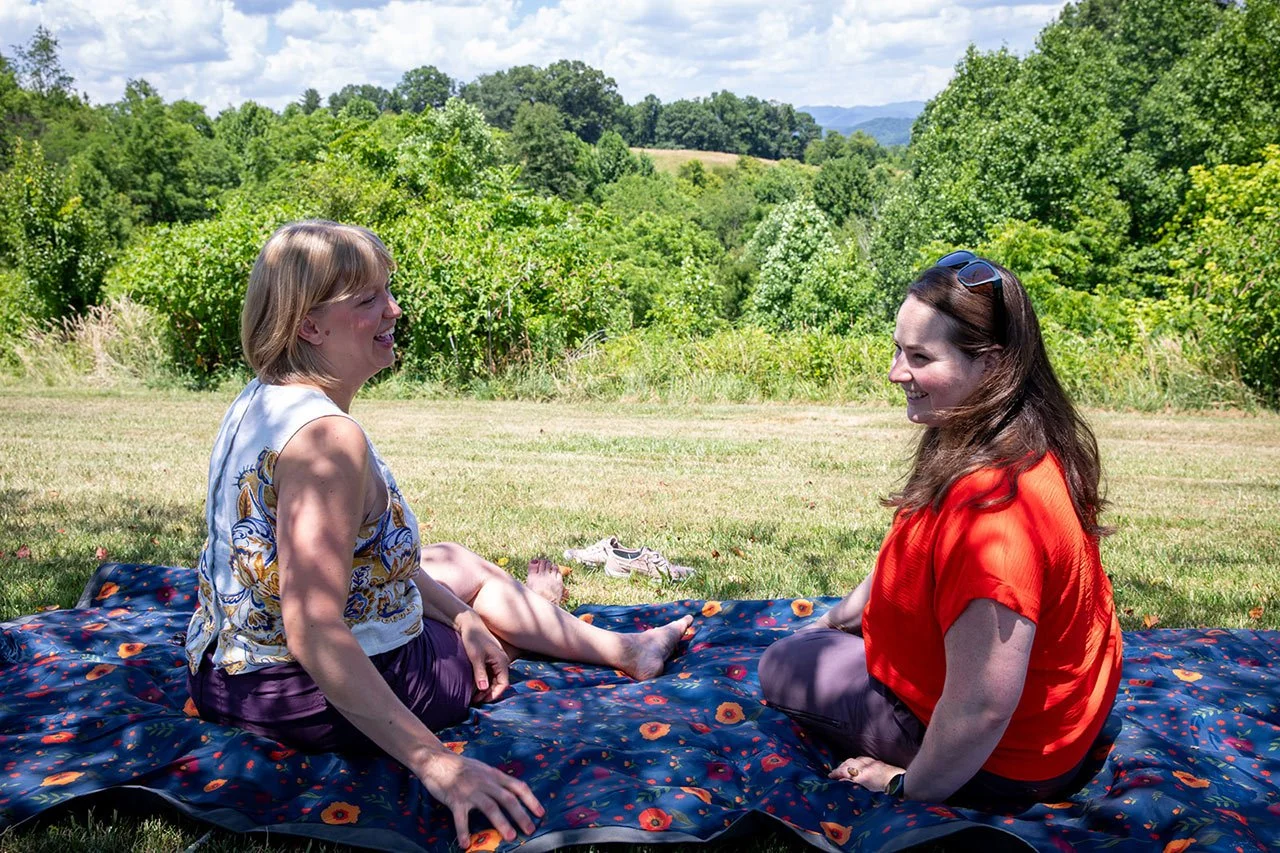Ginelle Krummey Asheville area therapist sits with client on picnic blanket in beautiful outdoor retreat setting