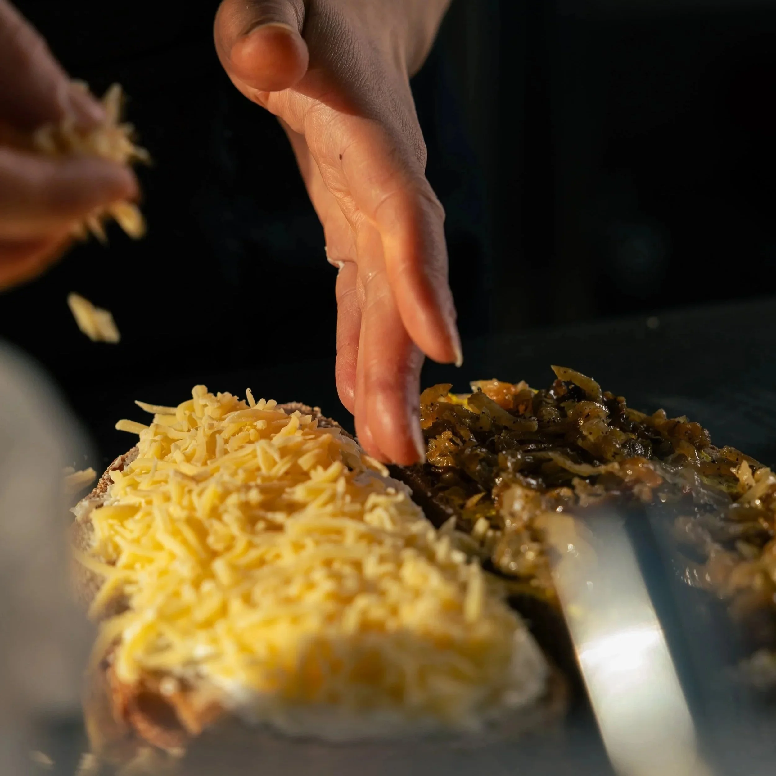 Nahaufnahme von einer Hand, die Käse und eine Hackfleisch- und Gemüsemischung auf einem Pizza-Teig verteilt.