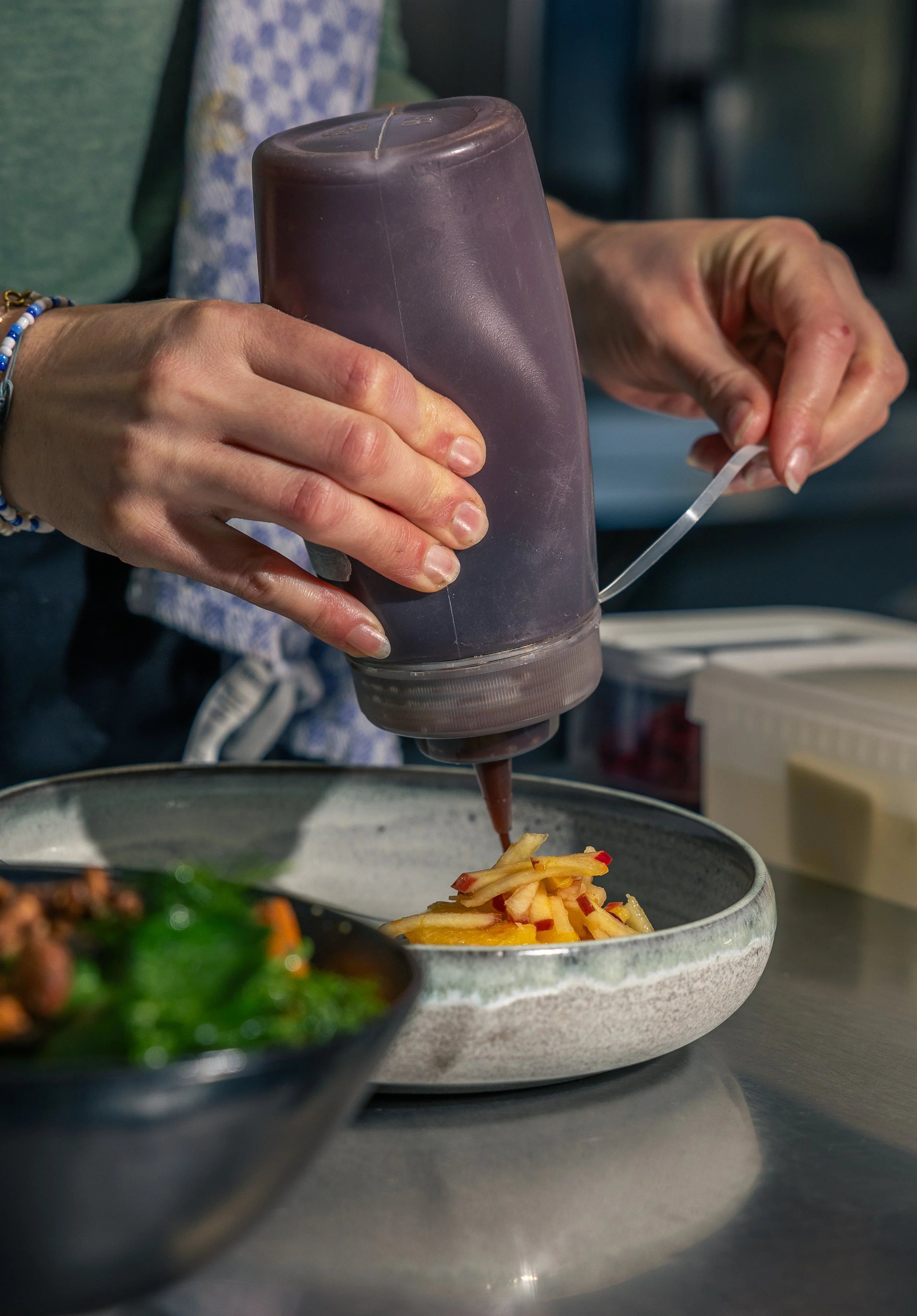 Eine Hand drück aus einer Spritztube Apfel-Pflaumen-Mus auf einen Teller mit marinierten Früchten.