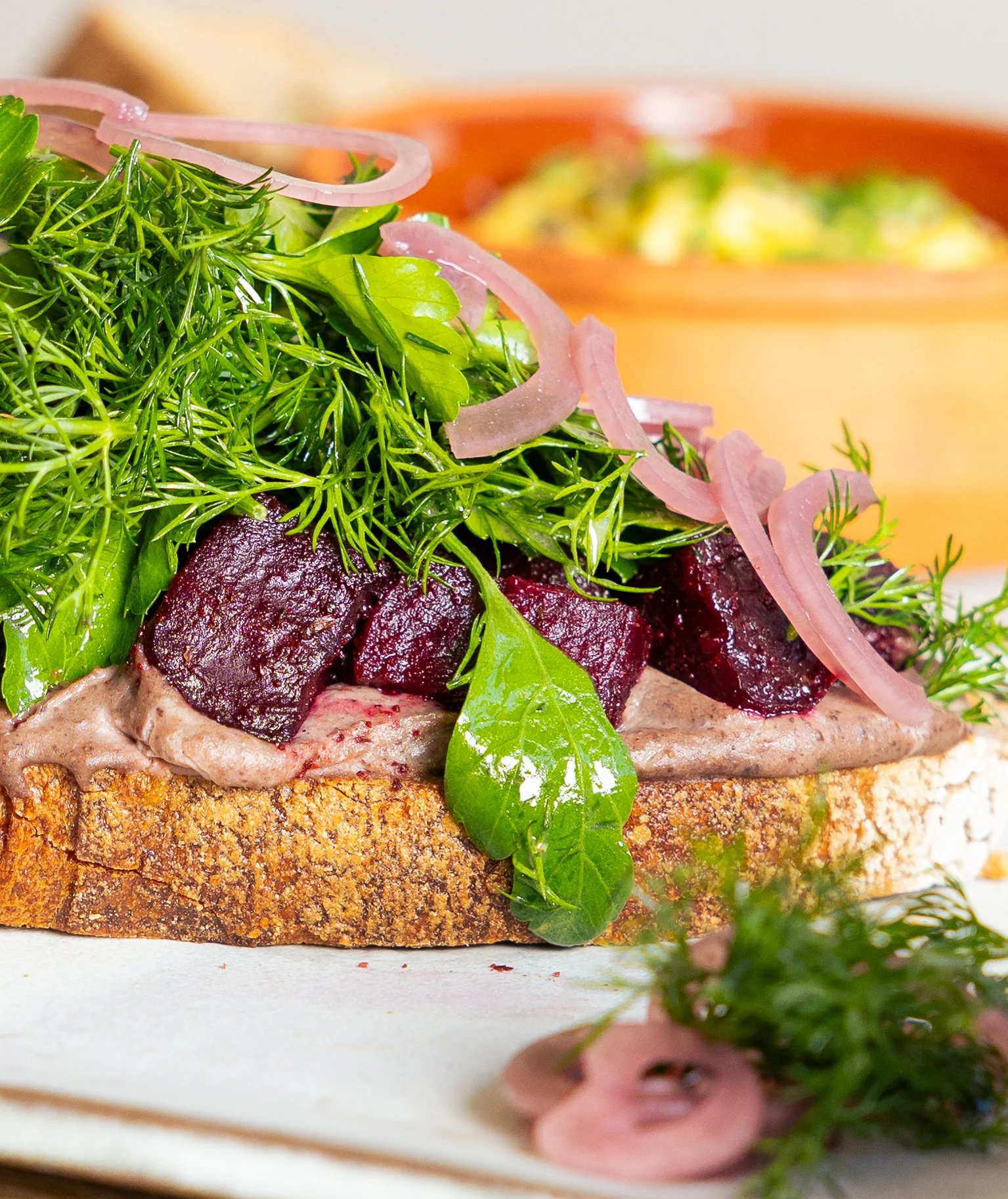 Schwarzer Bohnen Hummmus mit gerösteter Rote Bete auf einer Sauerteigstulle. Mit frischen Kräutersalat und eingelegten Zwiebeln.