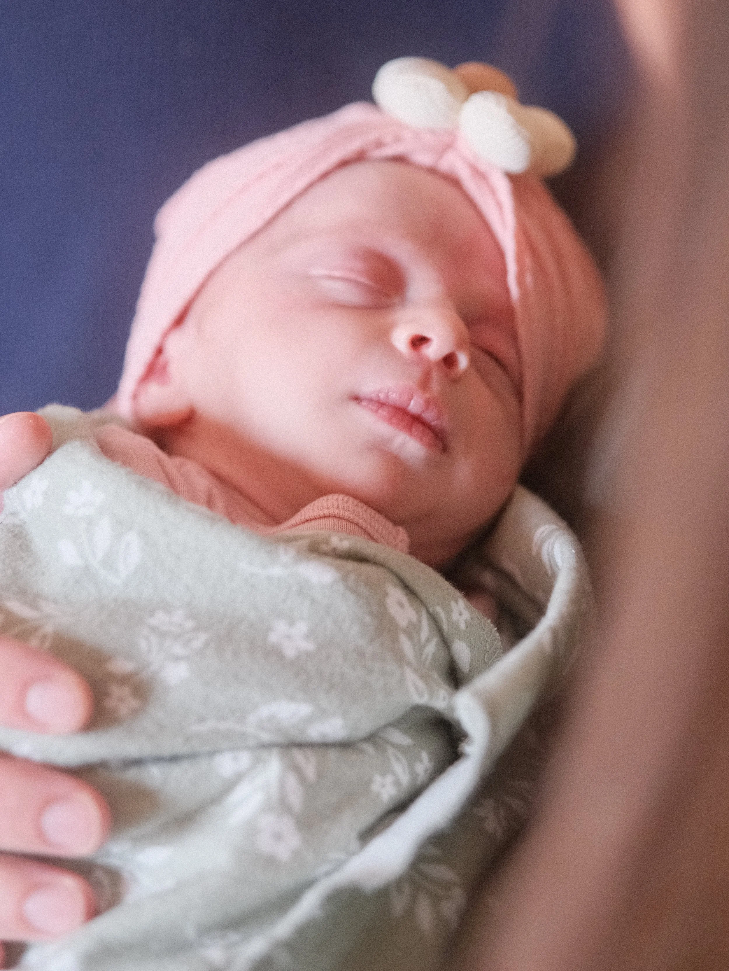 Close-up newborn baby portrait in Roanoke, Virginia, with her eyes peacefully closed, swaddled in a soft green and white blanket and wearing a pink headband.