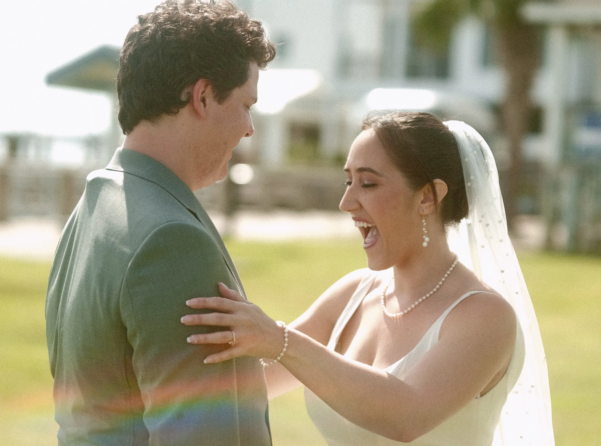 A bride smiling seeing her groom for the first time. Her hand is on his arm and her veil is behind her.
