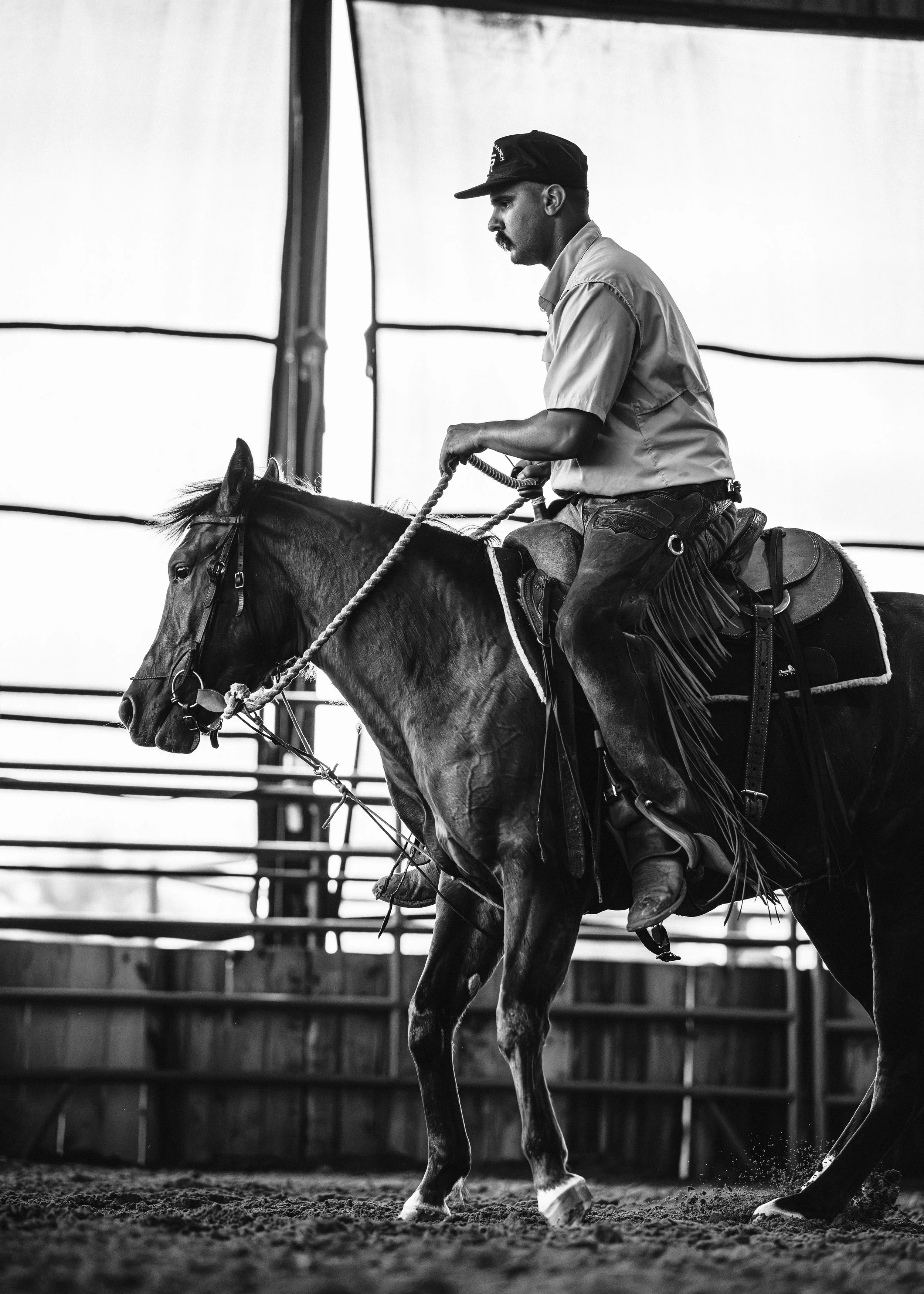 A man riding a horse inside a wooden structure, black and white photo.