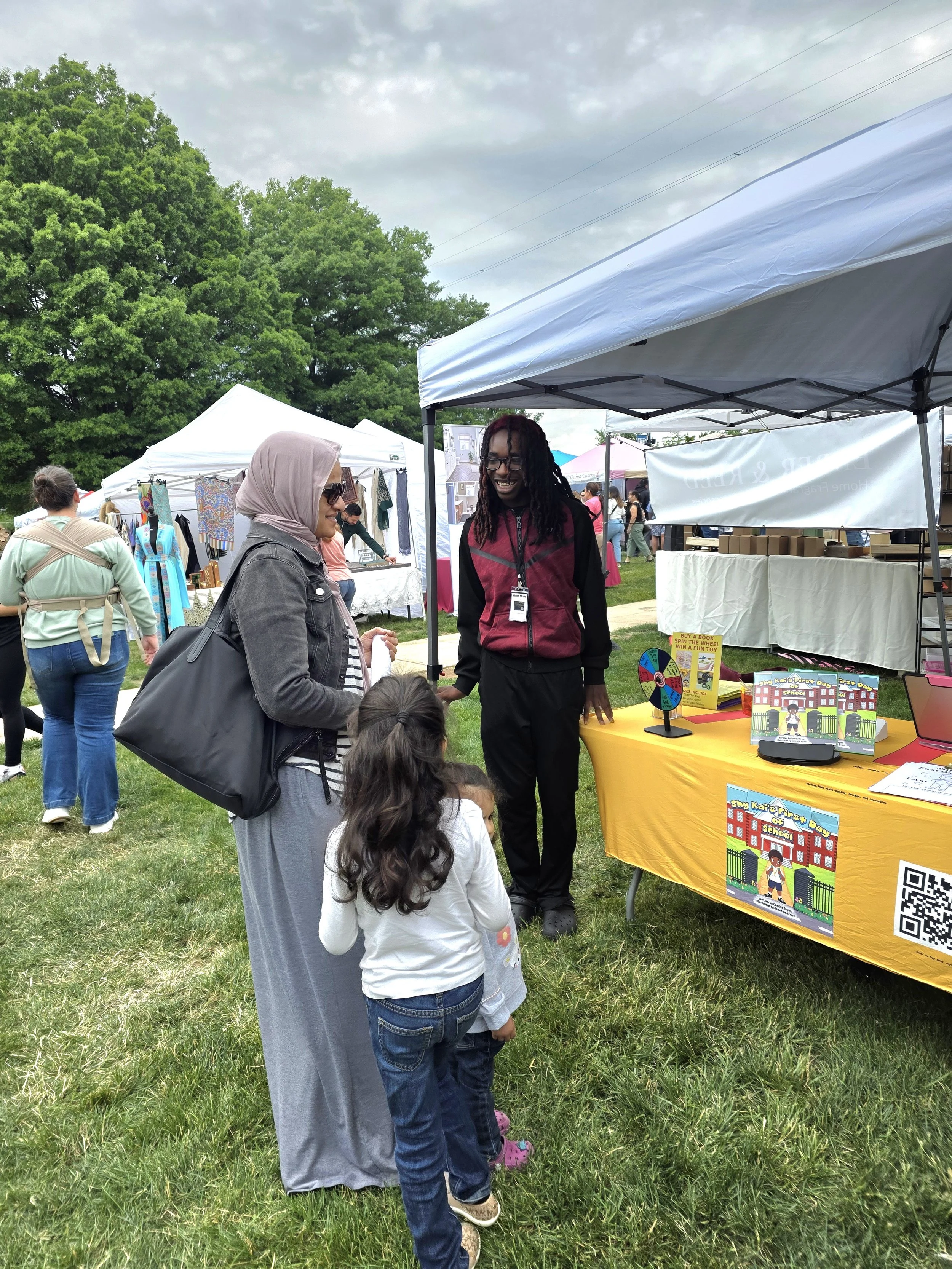 Kai talking with a mother and daughter about Shy Kai’s First Day of School at a family-friendly community vendor event.