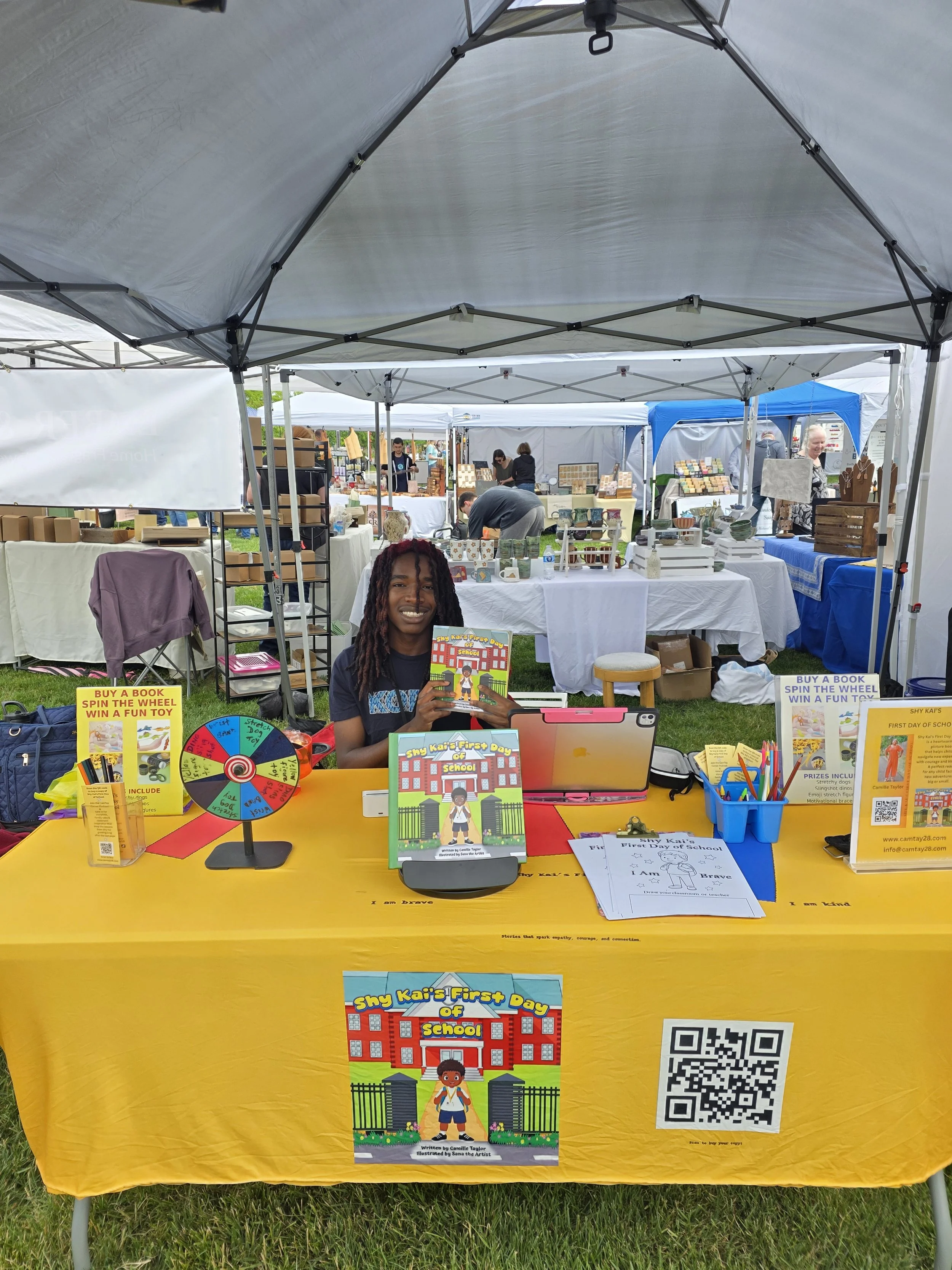 Kai at our vendor table promoting and selling Shy Kai’s First Day of School at a local community vendor event for children and families.