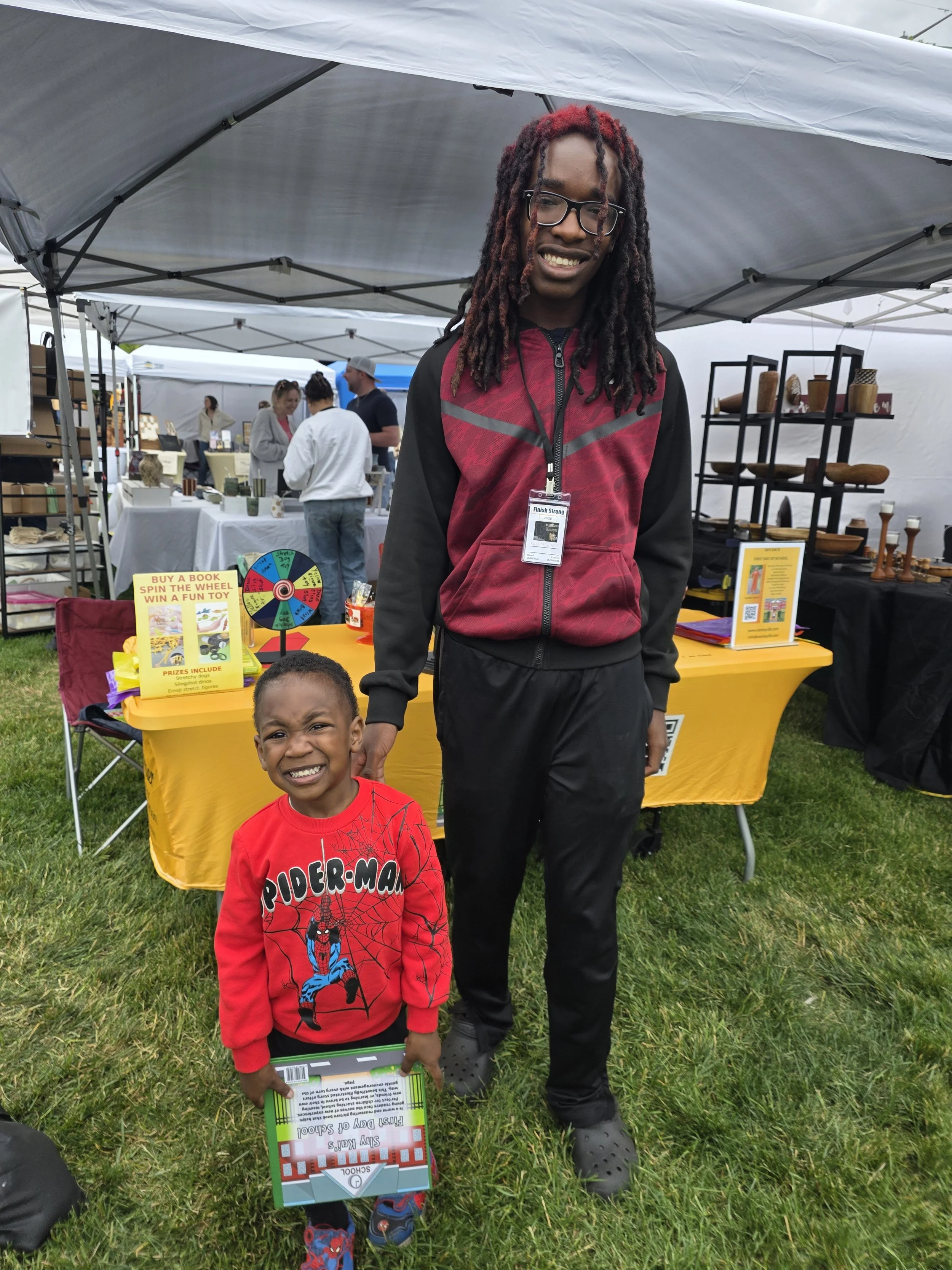 Kai standing with a young reader who purchased Shy Kai’s First Day of School at a local vendor event for families and children.