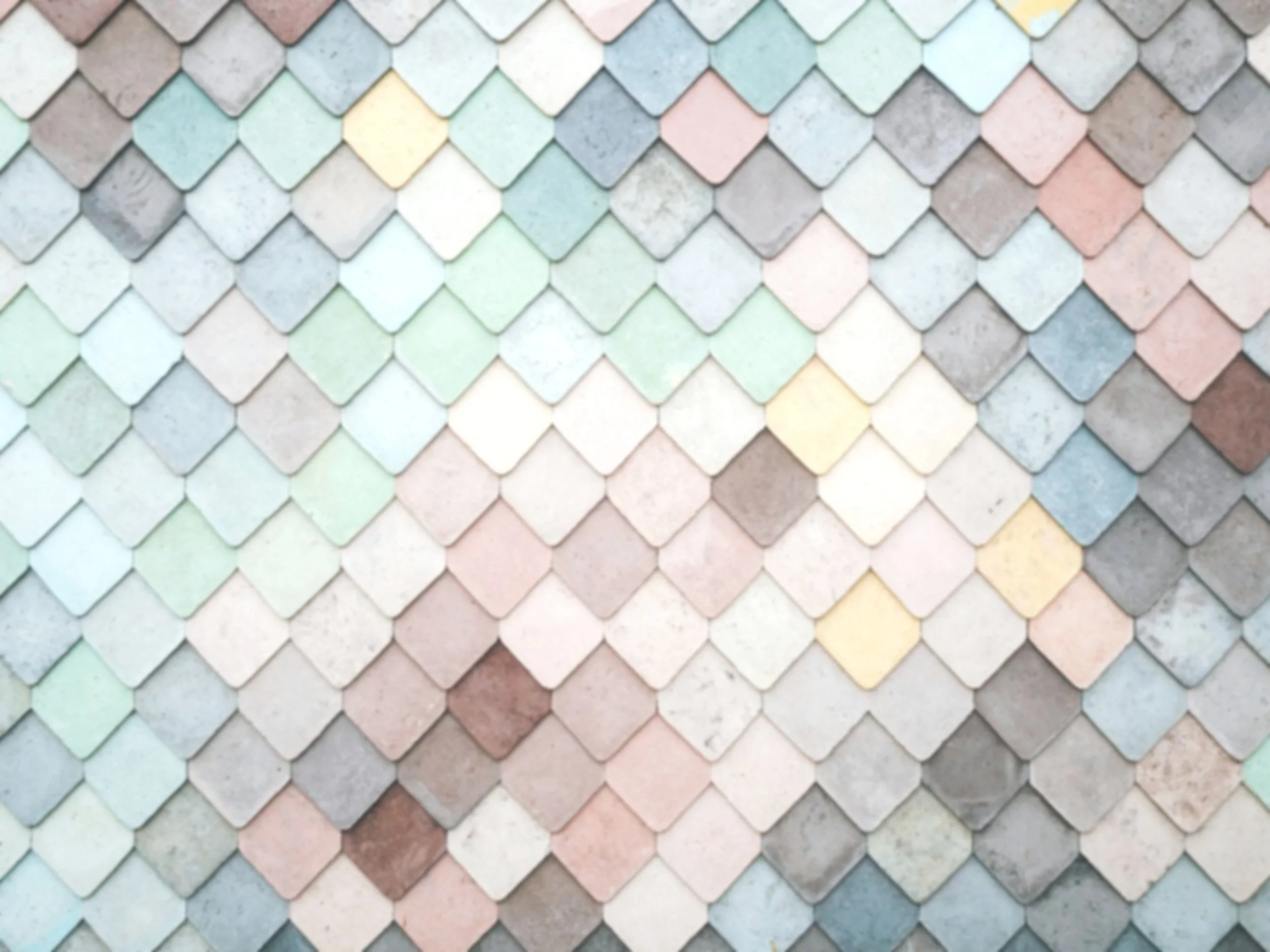 Close-up of a colorful tiled wall with diamond-shaped tiles in pastel shades of pink, blue, green, yellow, and gray, arranged in overlapping pattern.