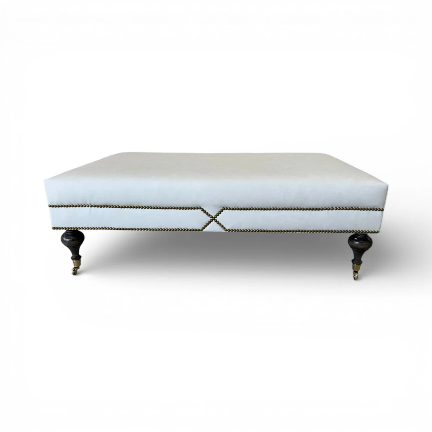 A white upholstered bench with dark wooden legs and bronze nailhead trim, set against a plain white background.