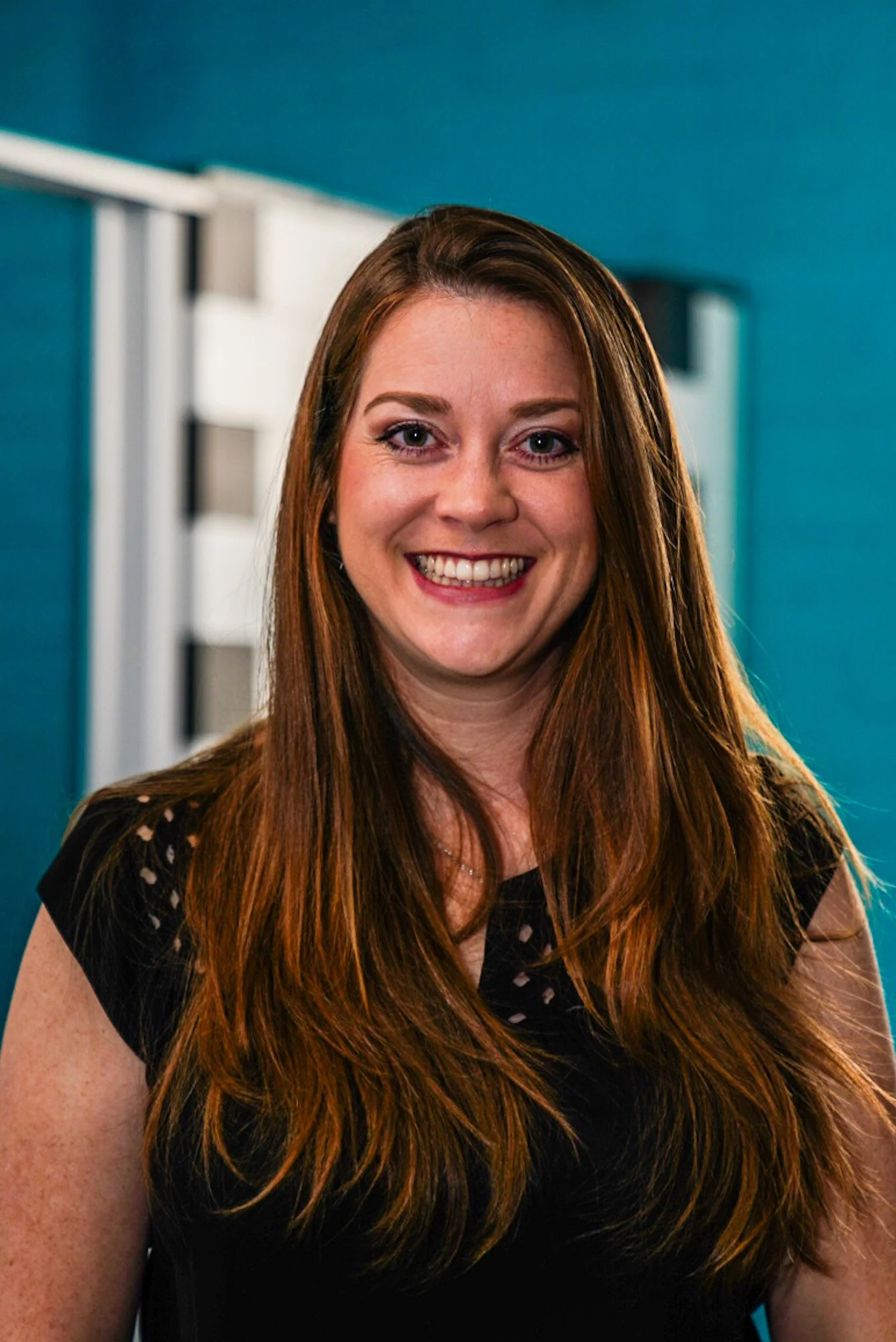 A woman with long, light brown hair smiling at the camera, wearing a black top with cut-out details.