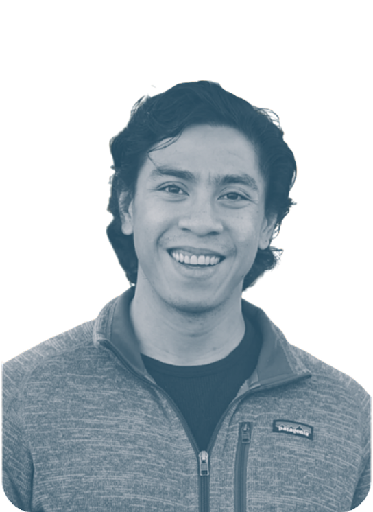 Portrait of a young man with dark wavy hair smiling, wearing a fleece jacket against a black background.