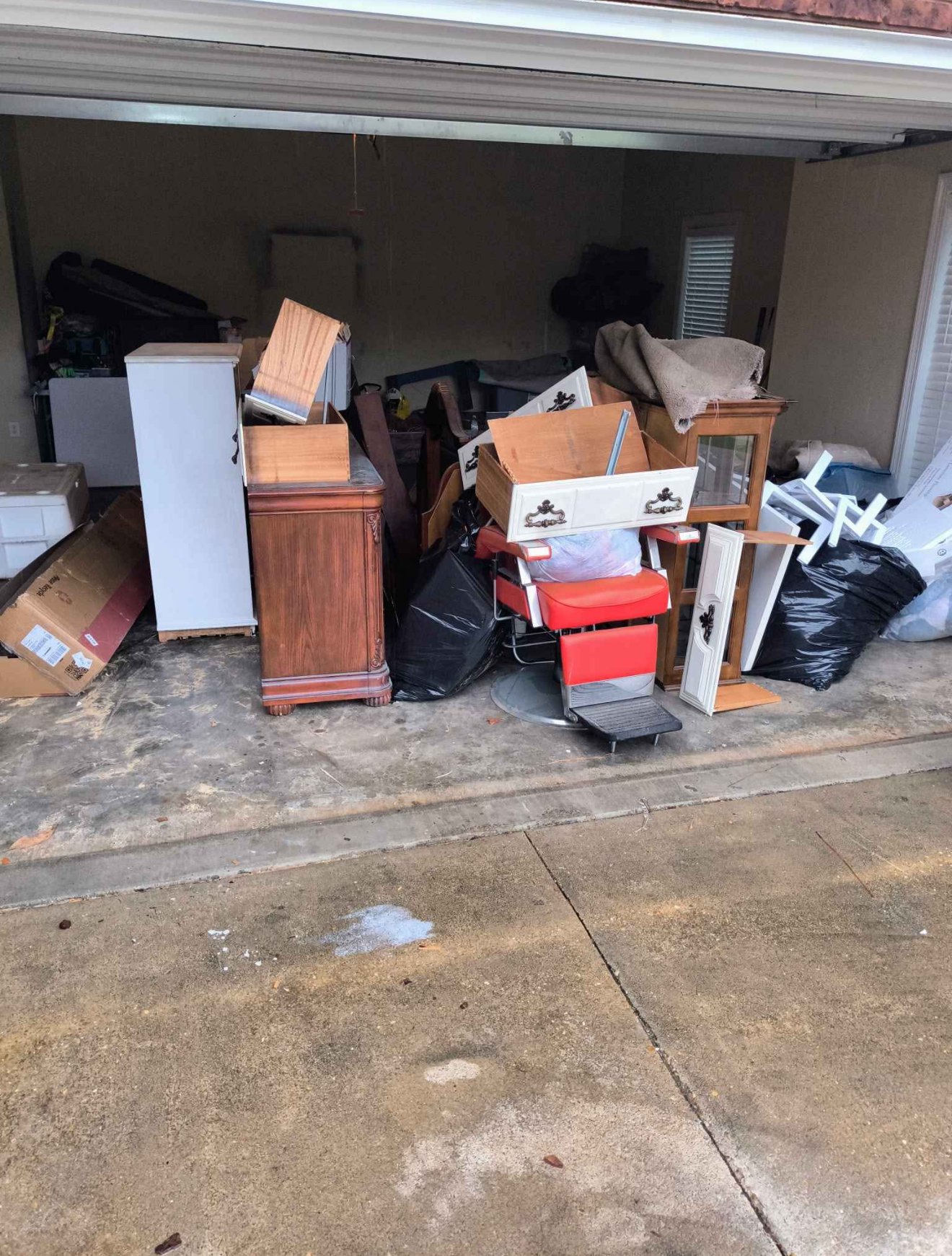 Garage filled with scattered furniture, boxes, and trash bags.