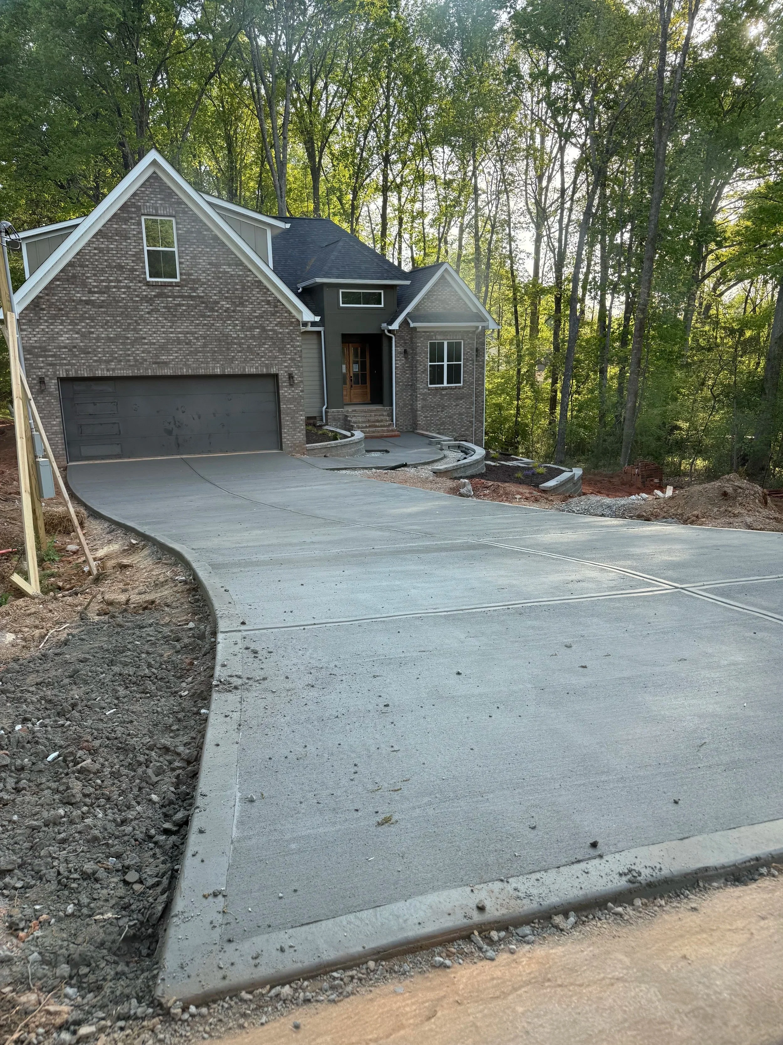 Newly constructed brick house with a concrete driveway leading to a two-car garage, surrounded by a wooded area in the background.