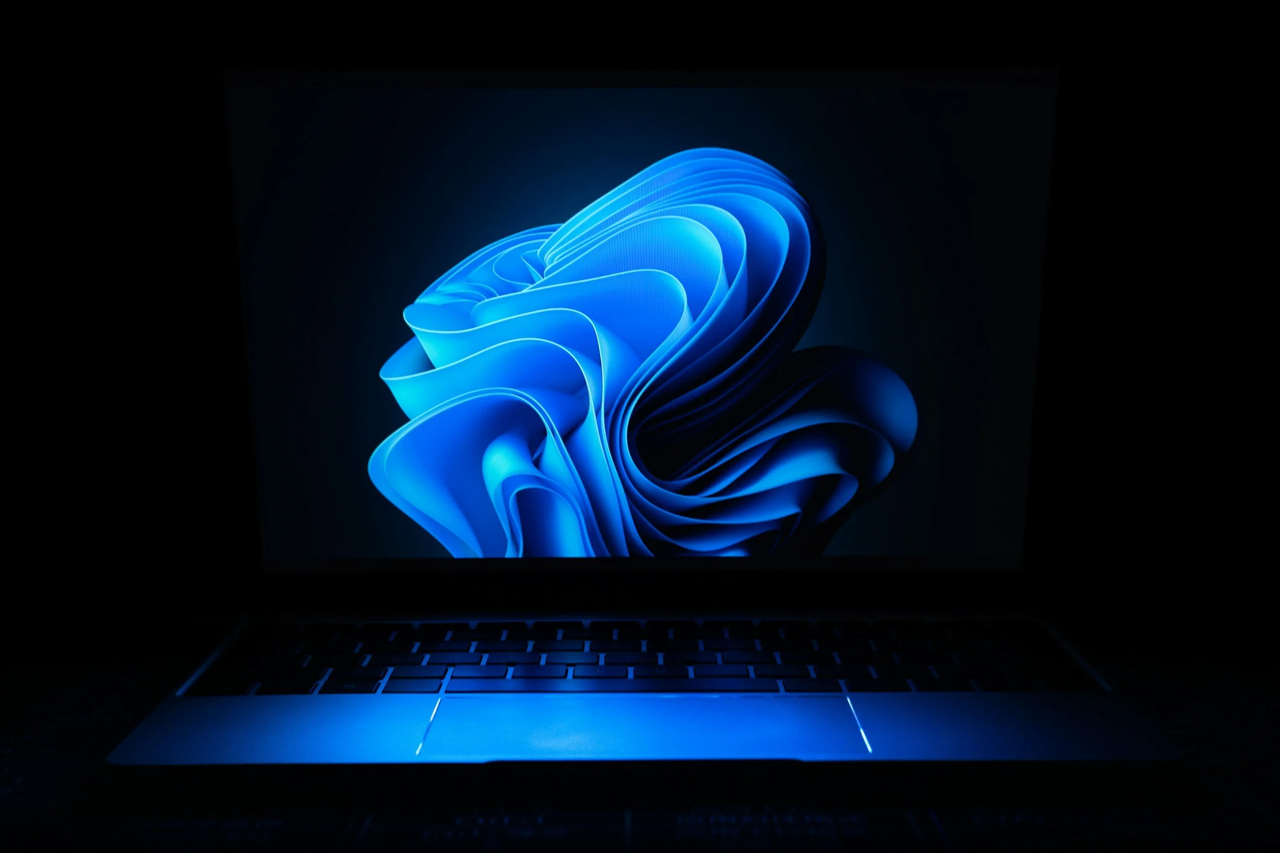 A laptop with a glowing blue abstract swirl design on the screen in a dark environment.