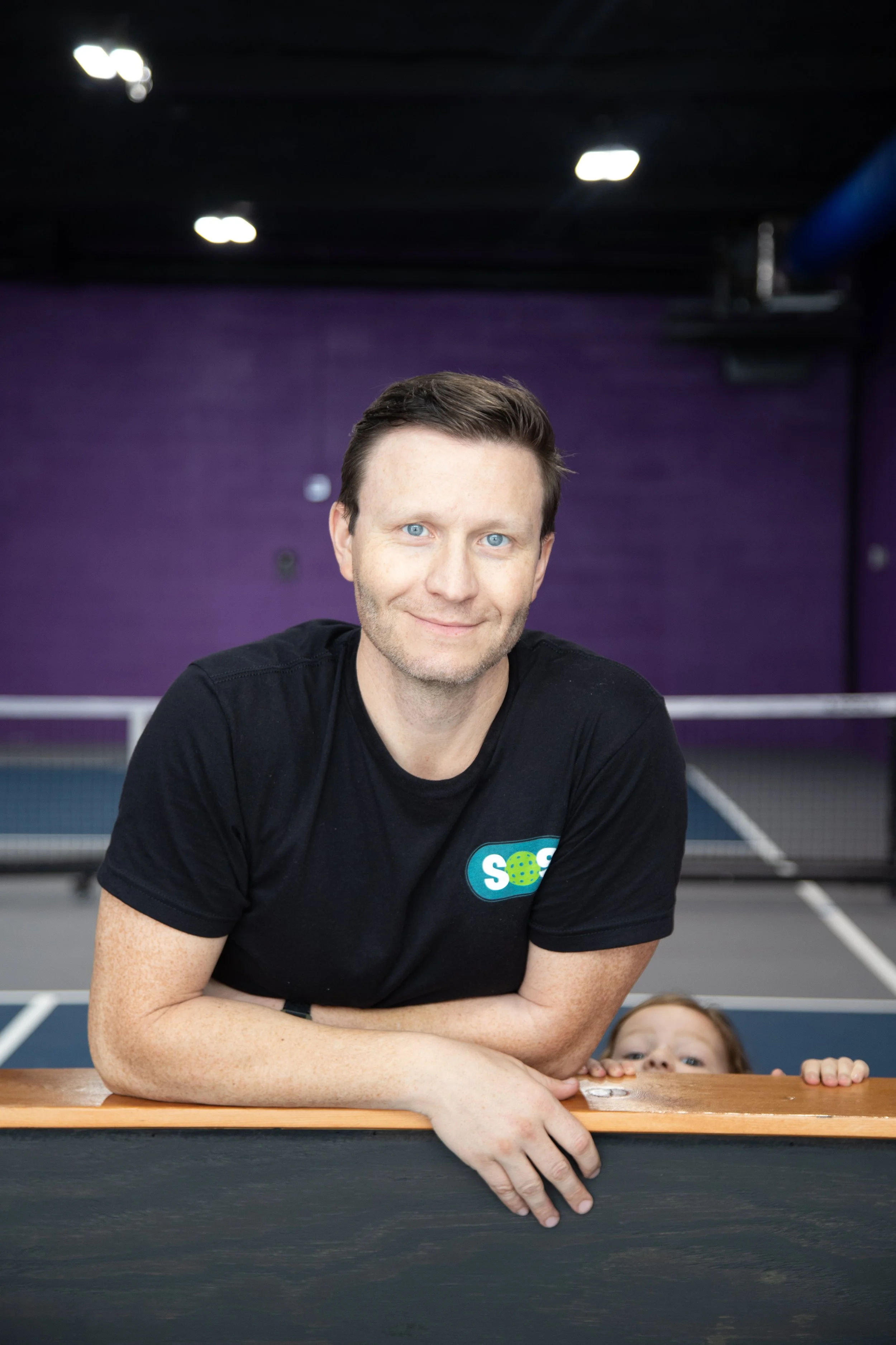 Young woman with a big smile, curly afro hairstyle, wearing glasses, hoop earrings, layered necklaces, and a striped shirt.