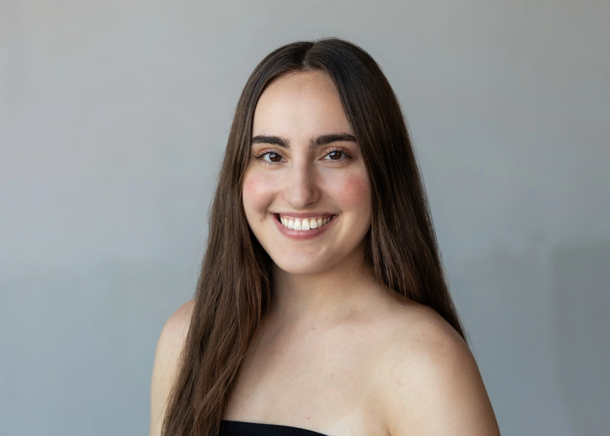 A smiling woman with long dark hair looks toward the camera against a light background.