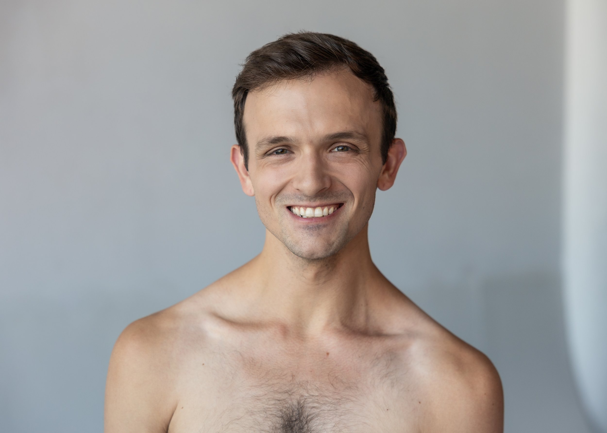 A smiling man looks directly at the camera against a light background.
