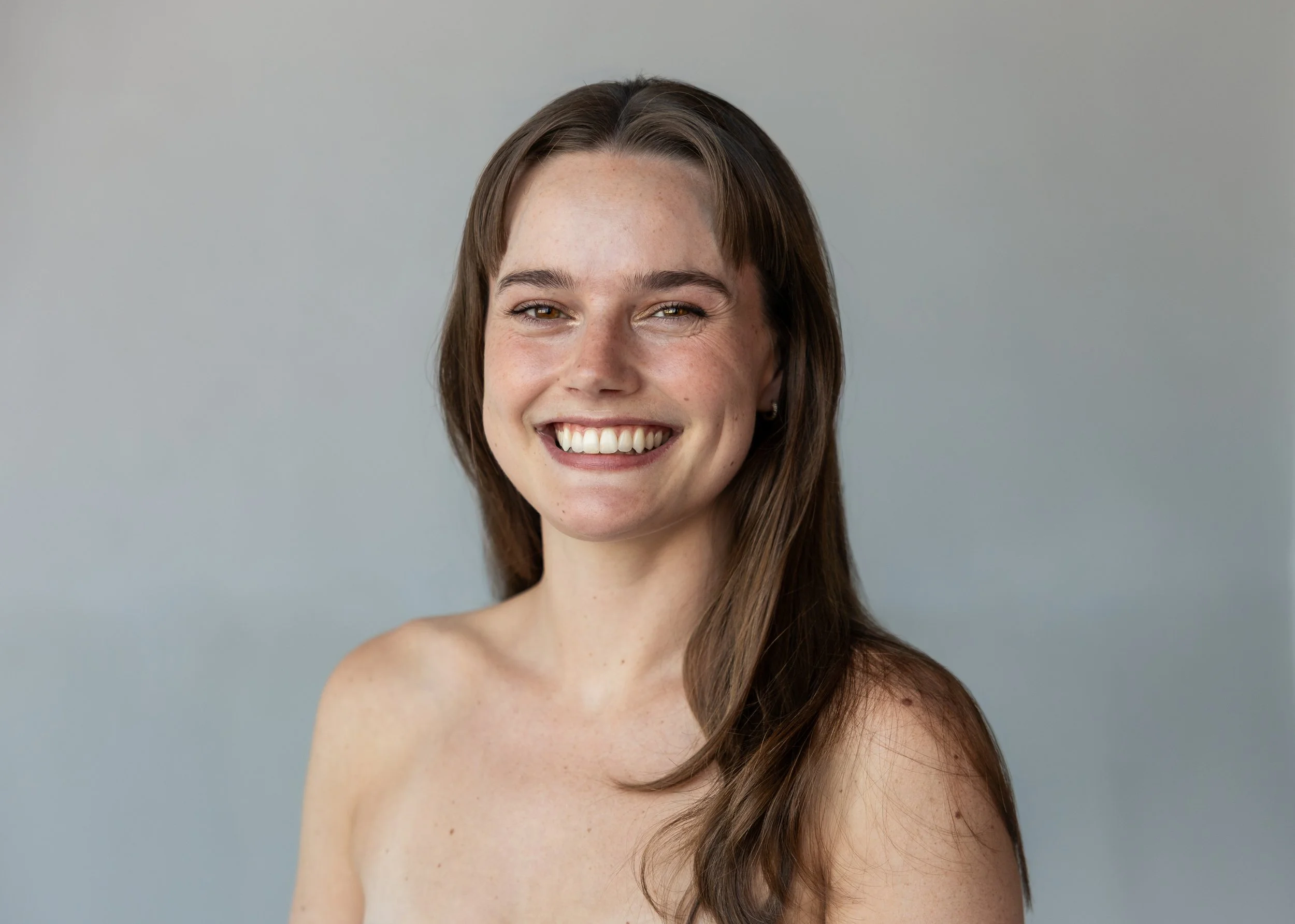 A smiling woman with long dark hair looks toward the camera against a light background.