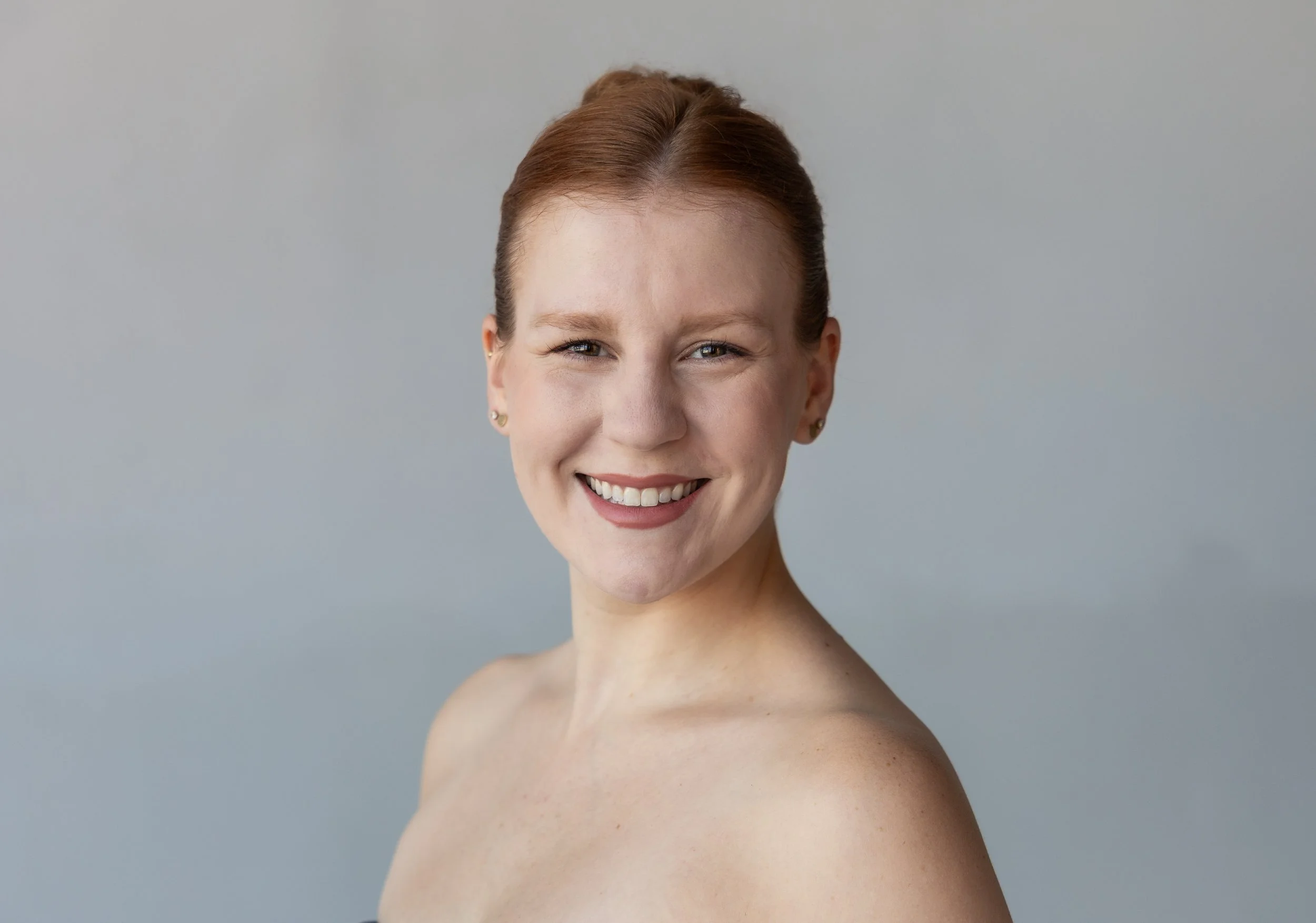 A smiling woman with red hair looks toward the camera against a light background.