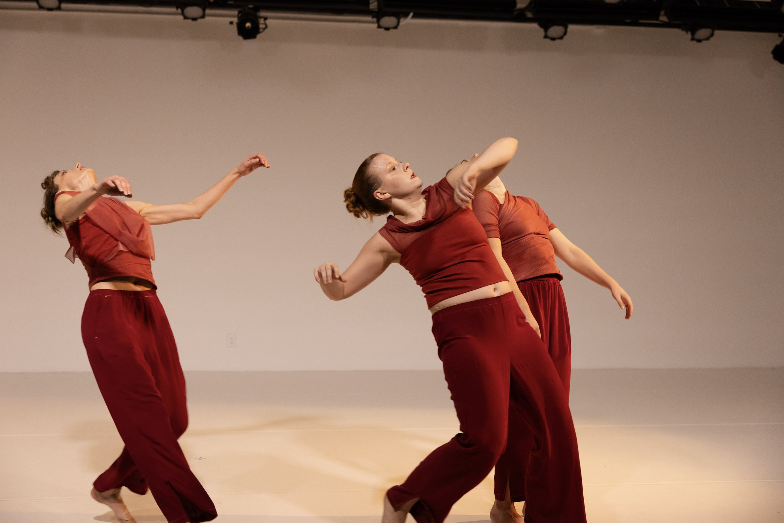 Three dancers lean and arc through space, torsos tilted and arms suspended mid-motion.