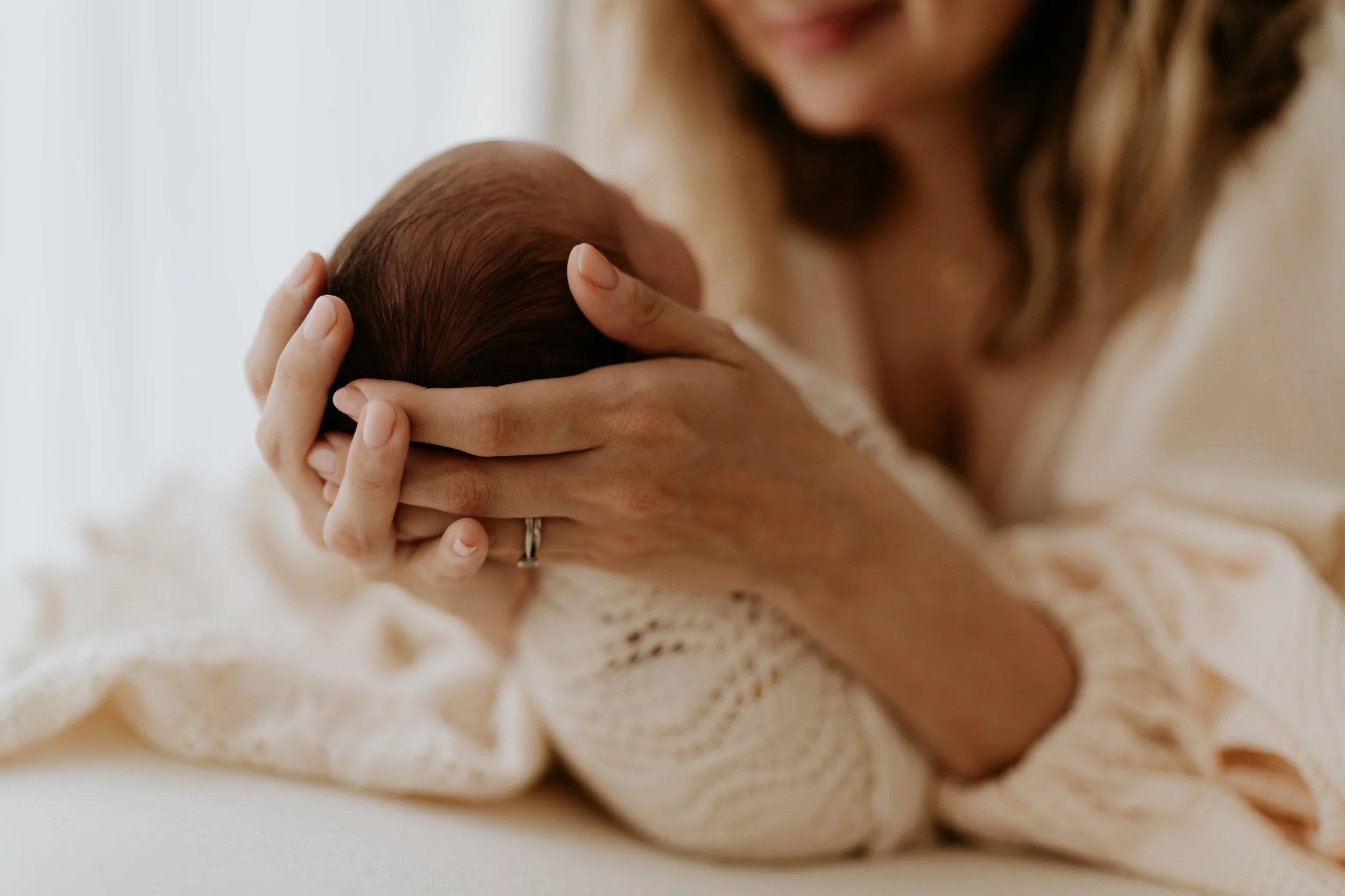 A woman cradling a newborn baby's head gently, close-up of her hands and the baby's head.