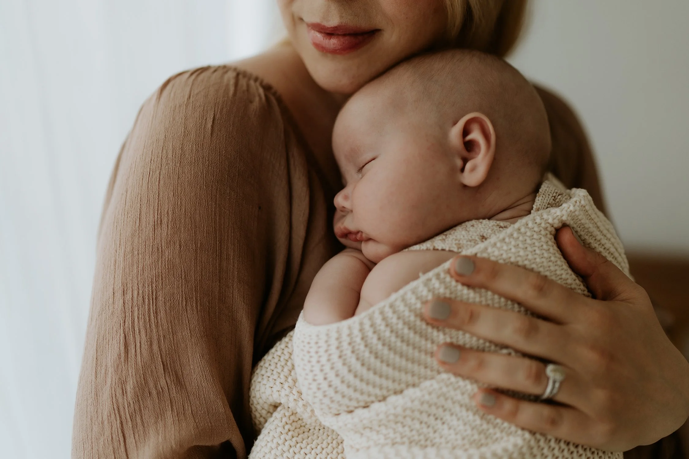 A woman holding a sleeping baby close to her chest, both resting peacefully indoors.