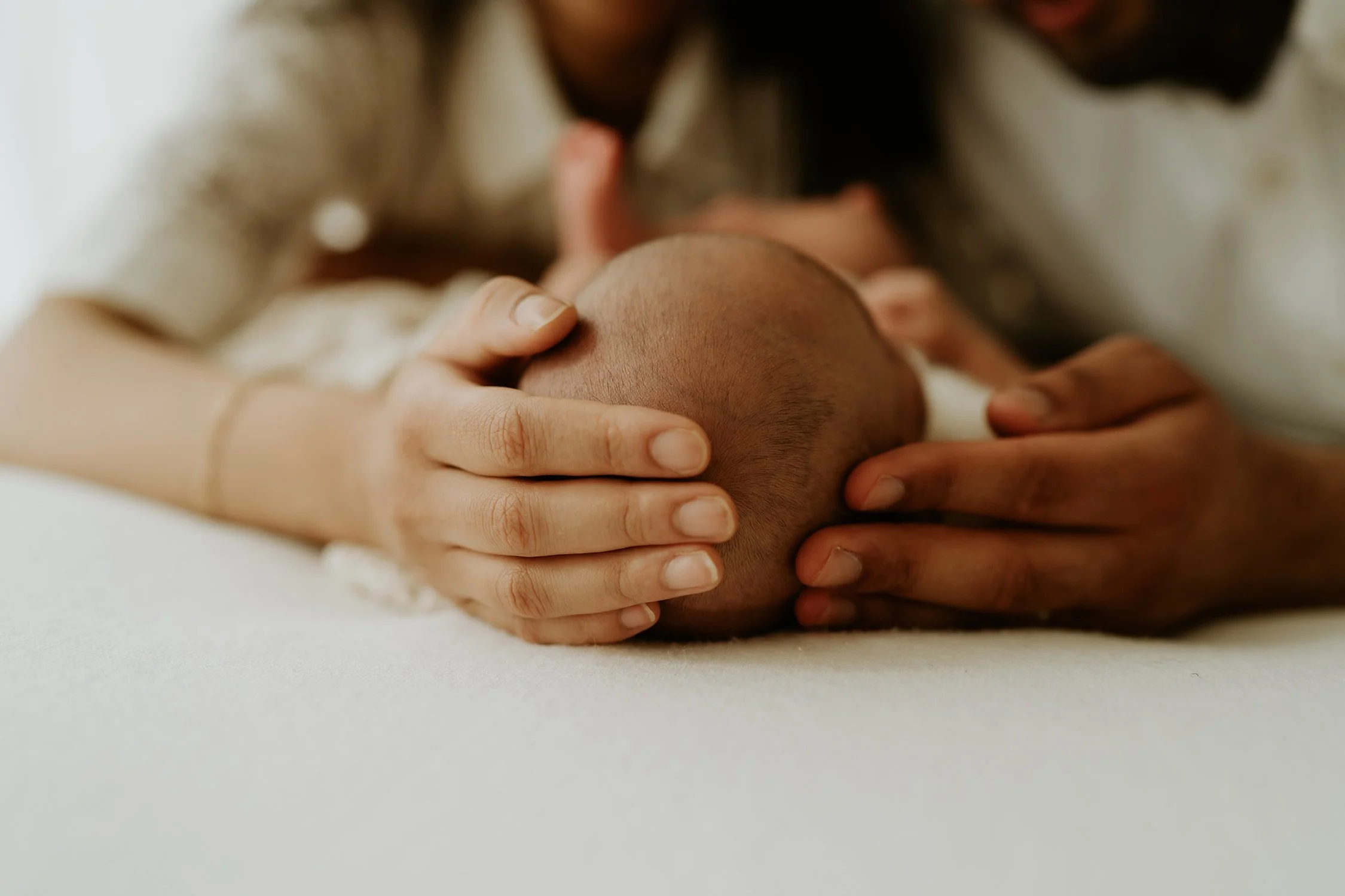 Person gently holding the head of a newborn baby with both hands, close-up of the baby's hair and the person's fingers.