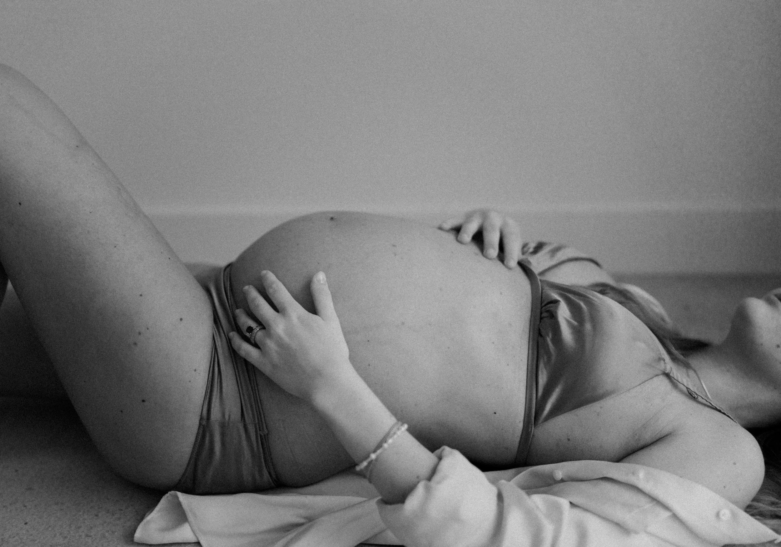 Black-and-white photo of a pregnant woman lying on her side, resting her hand on her belly, with her eyes closed.