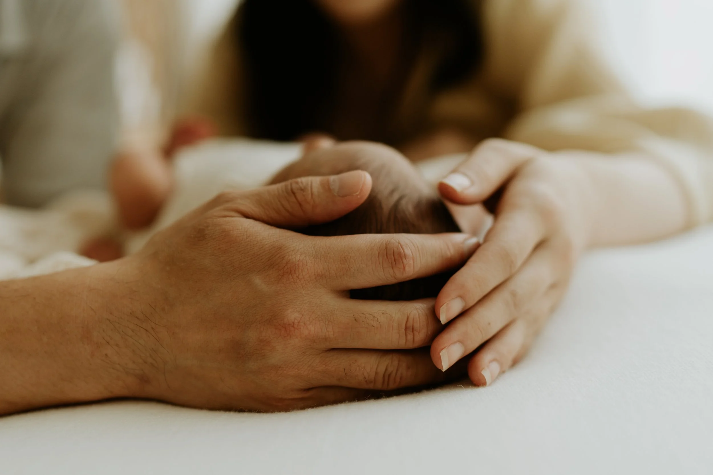 Close-up of adult hands gently holding a newborn baby's head with a blurred background.