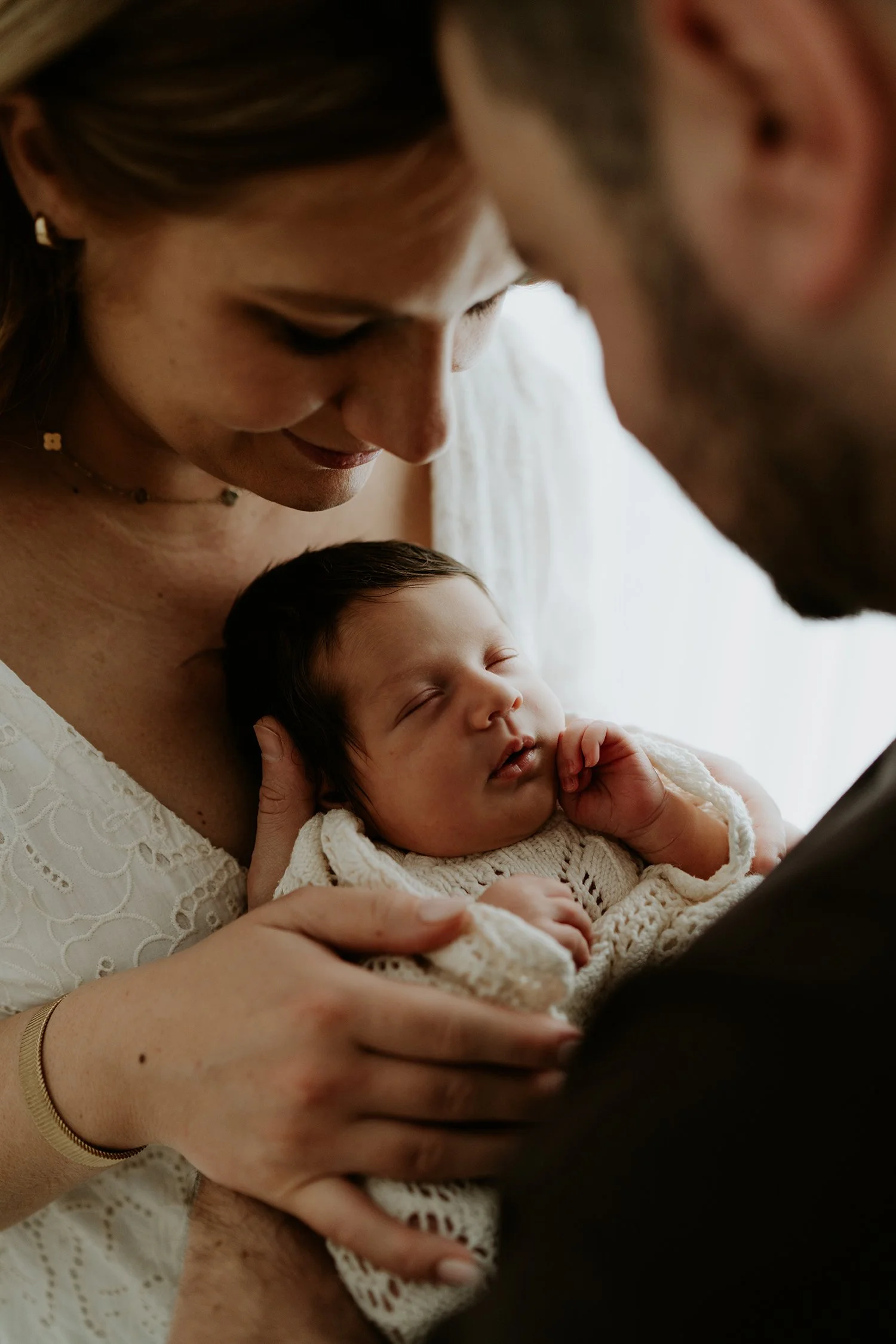 A woman and a man gently holding a sleeping baby.