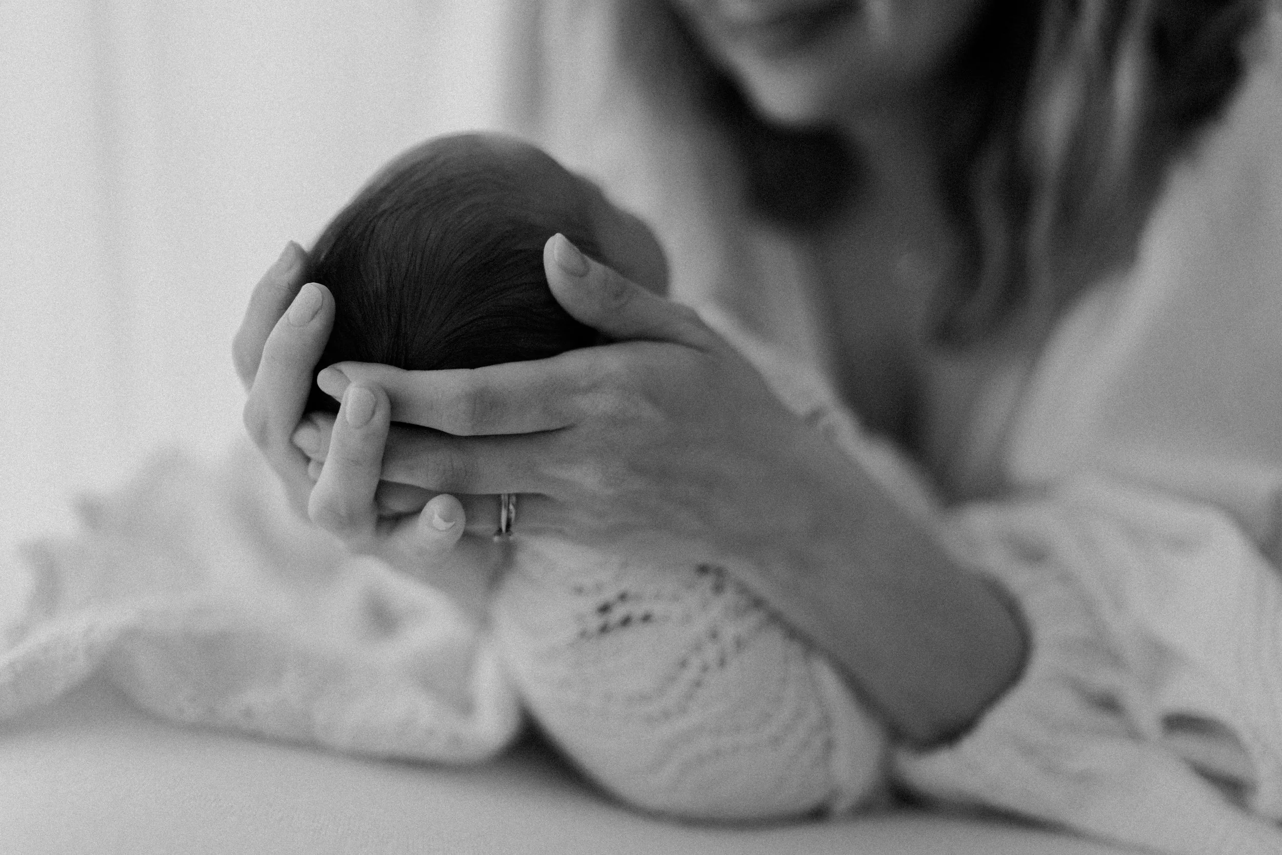 A woman gently holding a newborn baby's head in her hands, with her face partially visible.