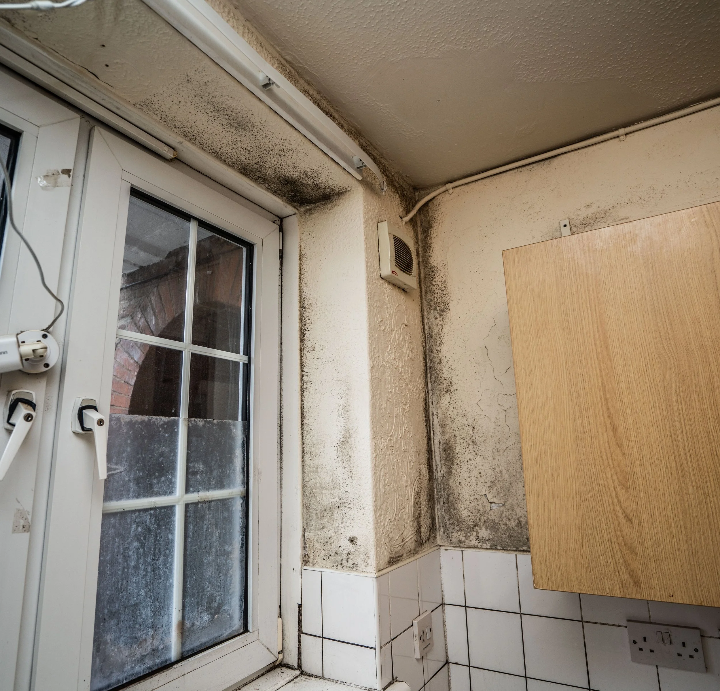 A dirty window with mold and grime buildup inside a room, near a ventilation system and electrical outlets.