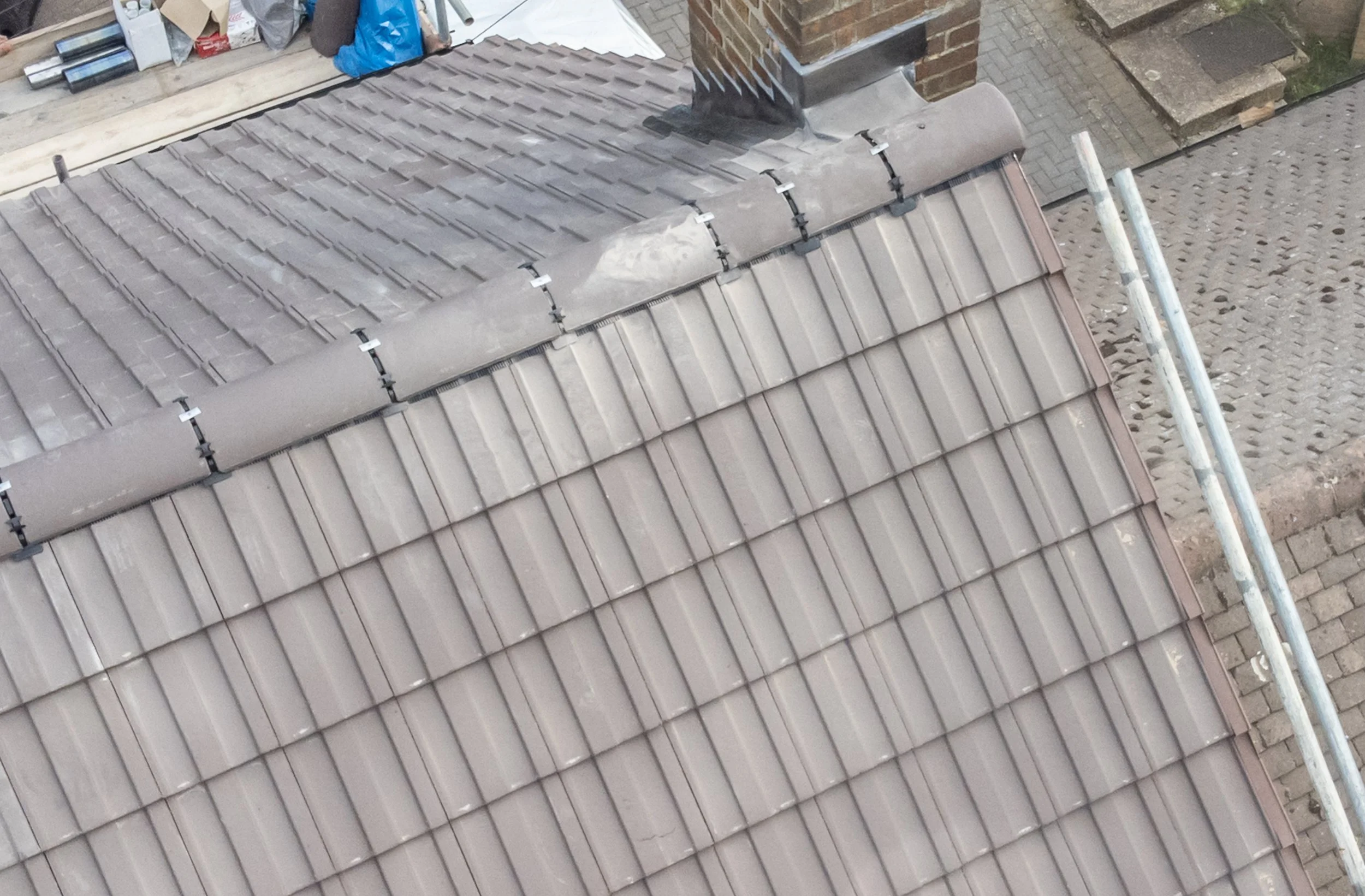Aerial view of a roof under construction with tiles, a chimney, and scaffolding.