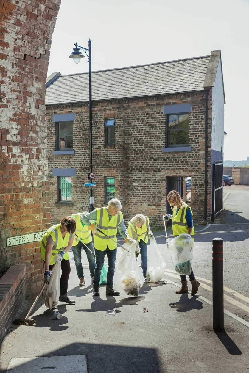 Group of five people wearing yellow safety vests picking up litter on a sidewalk during daylight.