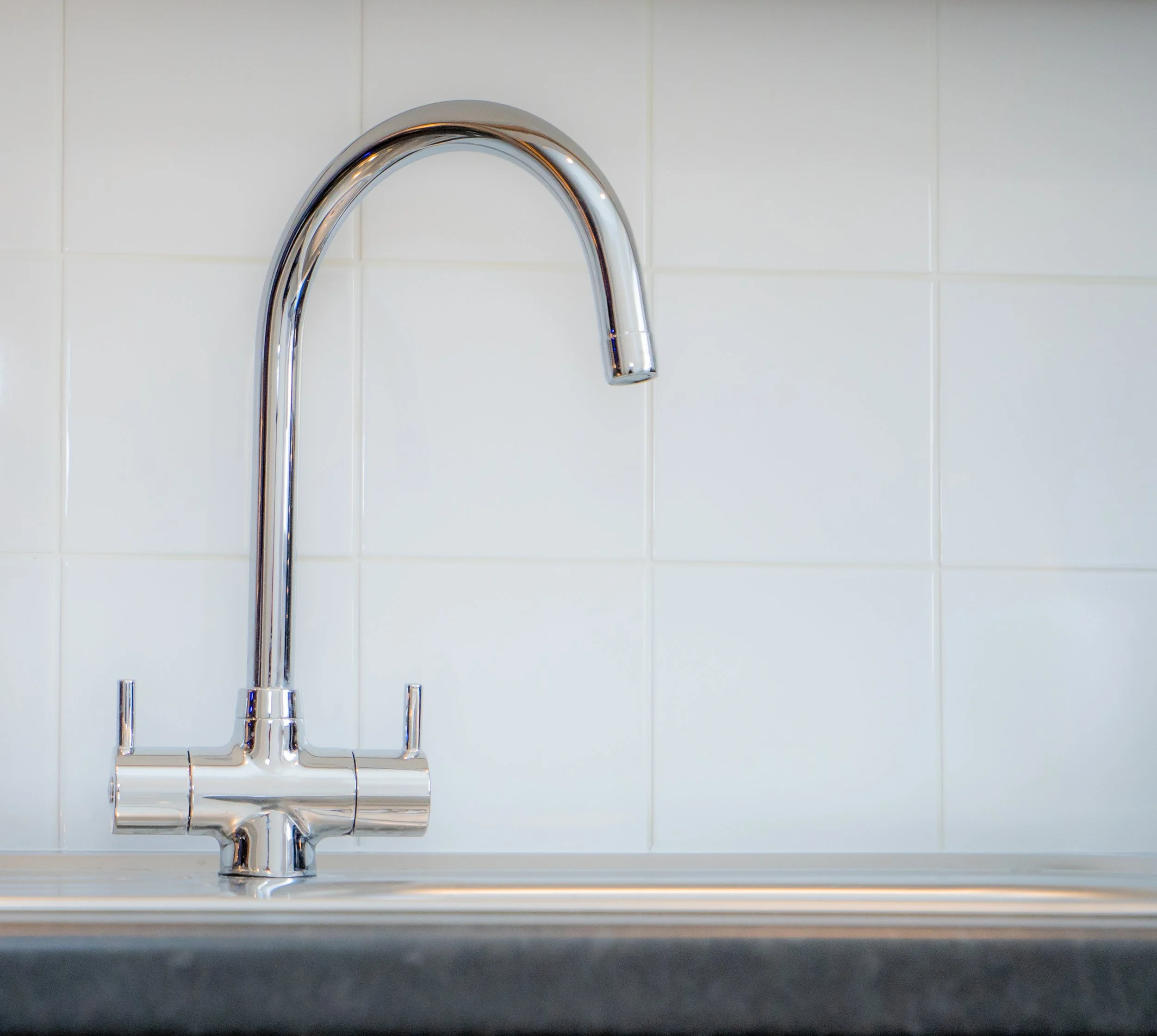 A chrome kitchen faucet mounted on a white tiled wall.