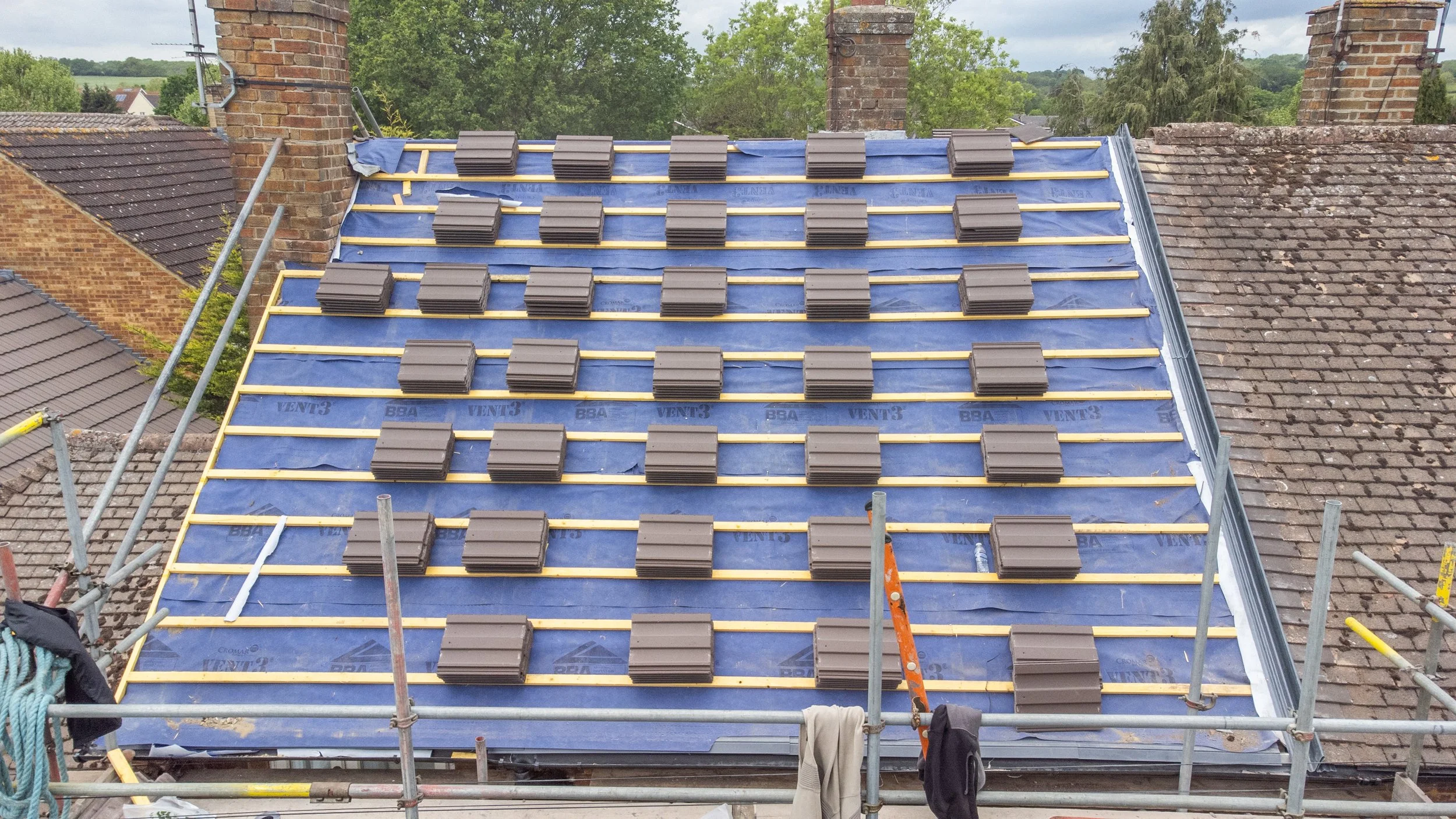 Construction scaffolding surrounding a house roof under renovation, with roof tiles stacked and waiting to be installed.