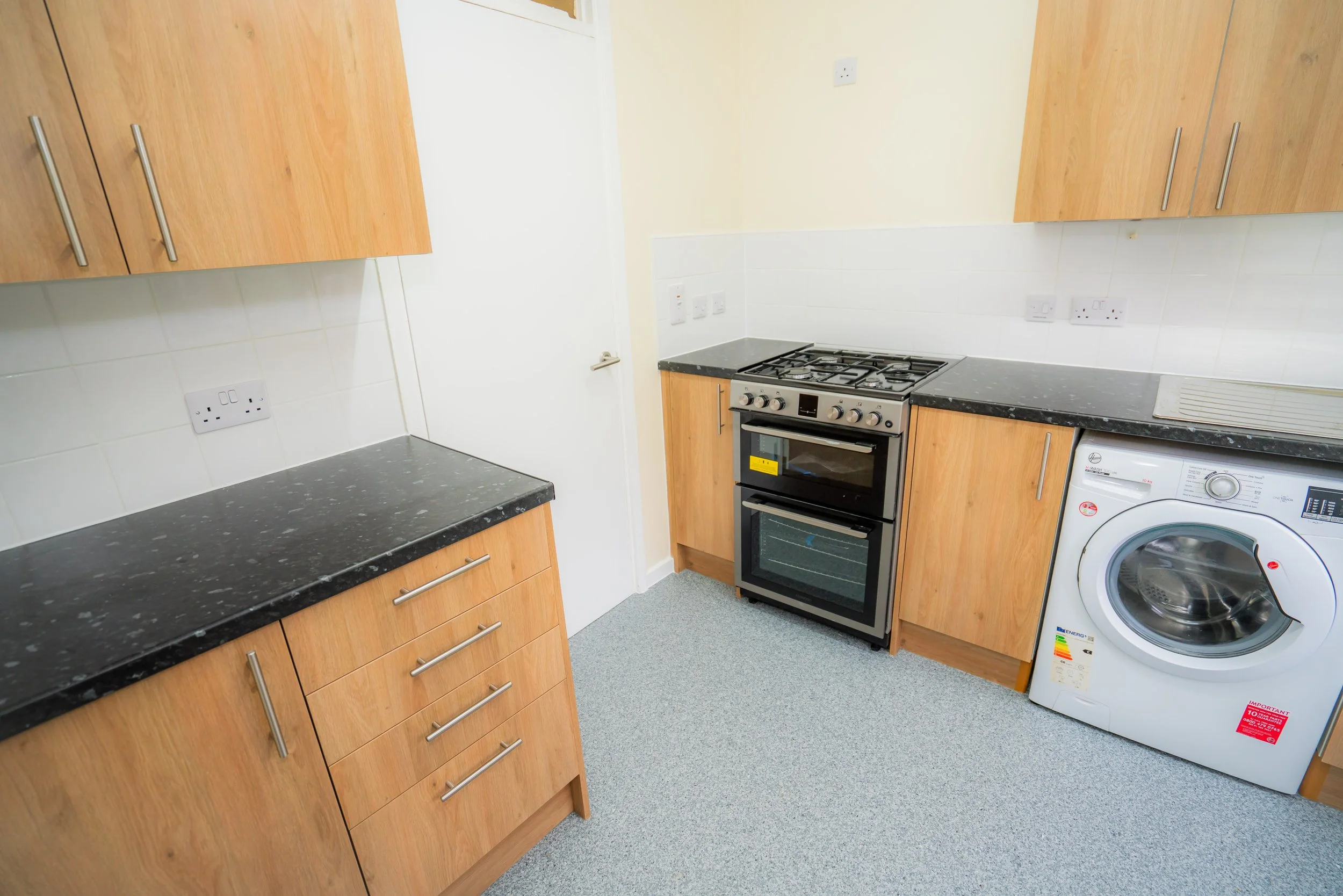Modern kitchen with white cabinets, wooden countertops, tile backsplash, and various appliances including a microwave, oven, kettle, and toaster.