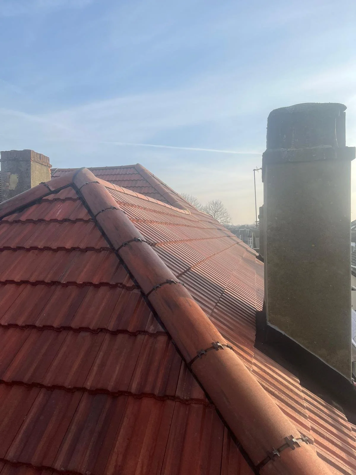 View of a red-tiled roof with chimney on a clear day with blue sky.