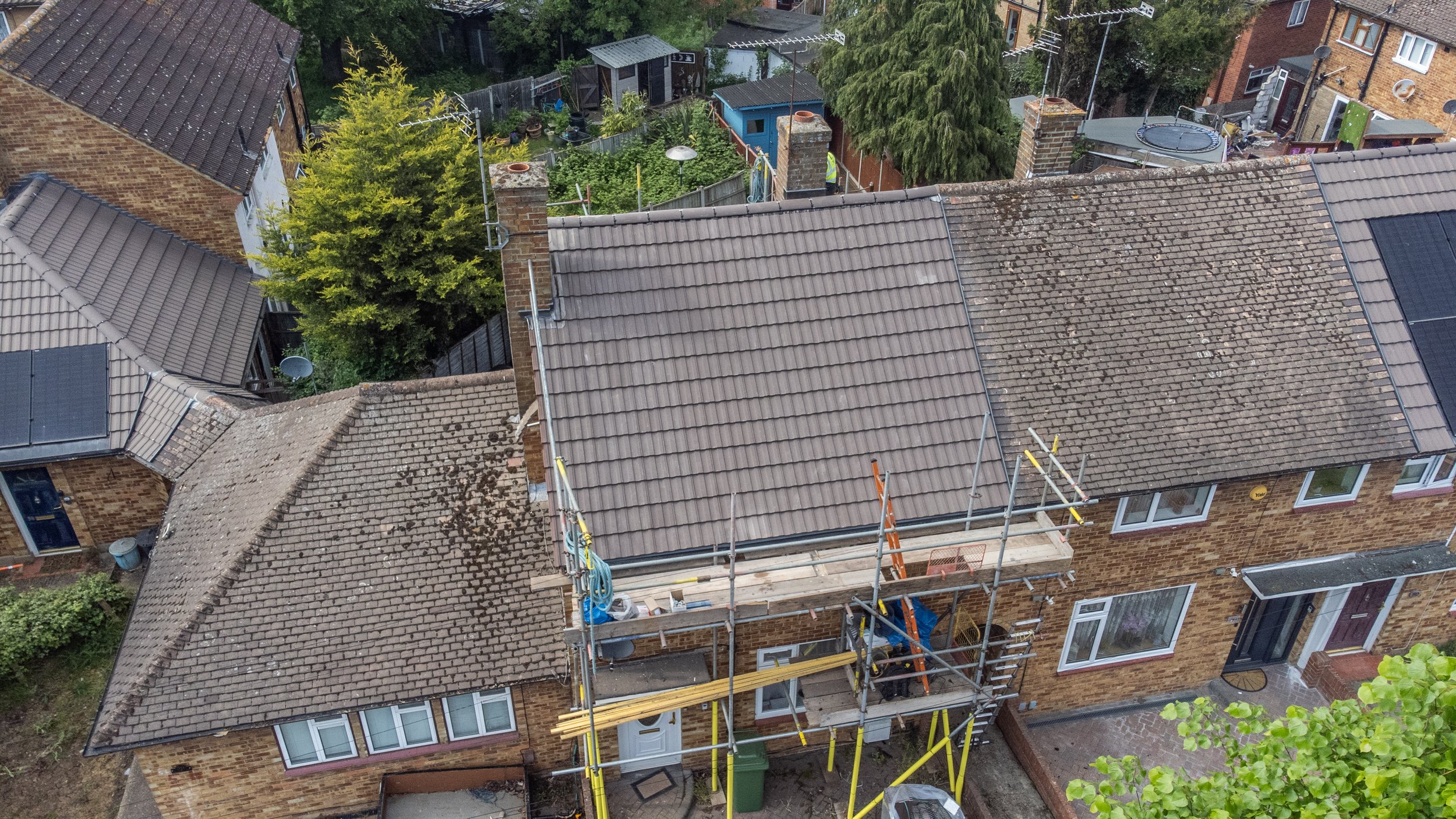 Aerial view of rooftops with ongoing roof renovations, scaffolding, and construction workers in a residential neighborhood.