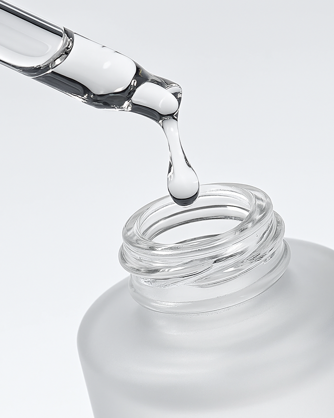 A glass dropper releasing a clear liquid into an open bottle with a white background.
