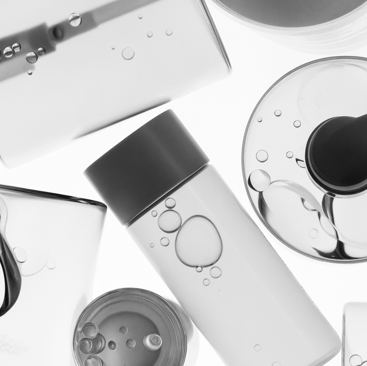 A collection of black and clear cosmetic bottles and containers with water droplets on them, arranged on a white background.