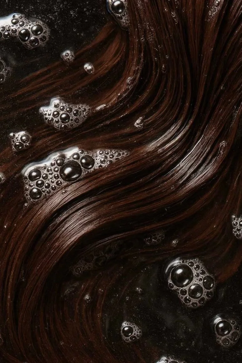 Close-up of dark brown, glossy hair with soap bubbles on its surface.